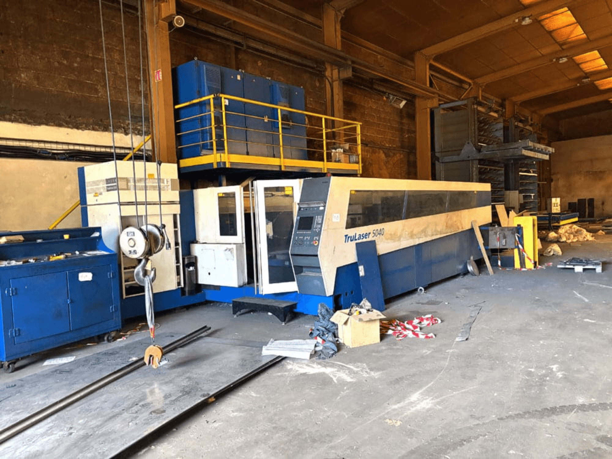 Máquina de corte a laser de CO₂ da TRUMPF, modelo TRULASER 5040, fotografada numa oficina, vista frontal em ângulo com um fundo desorganizado.