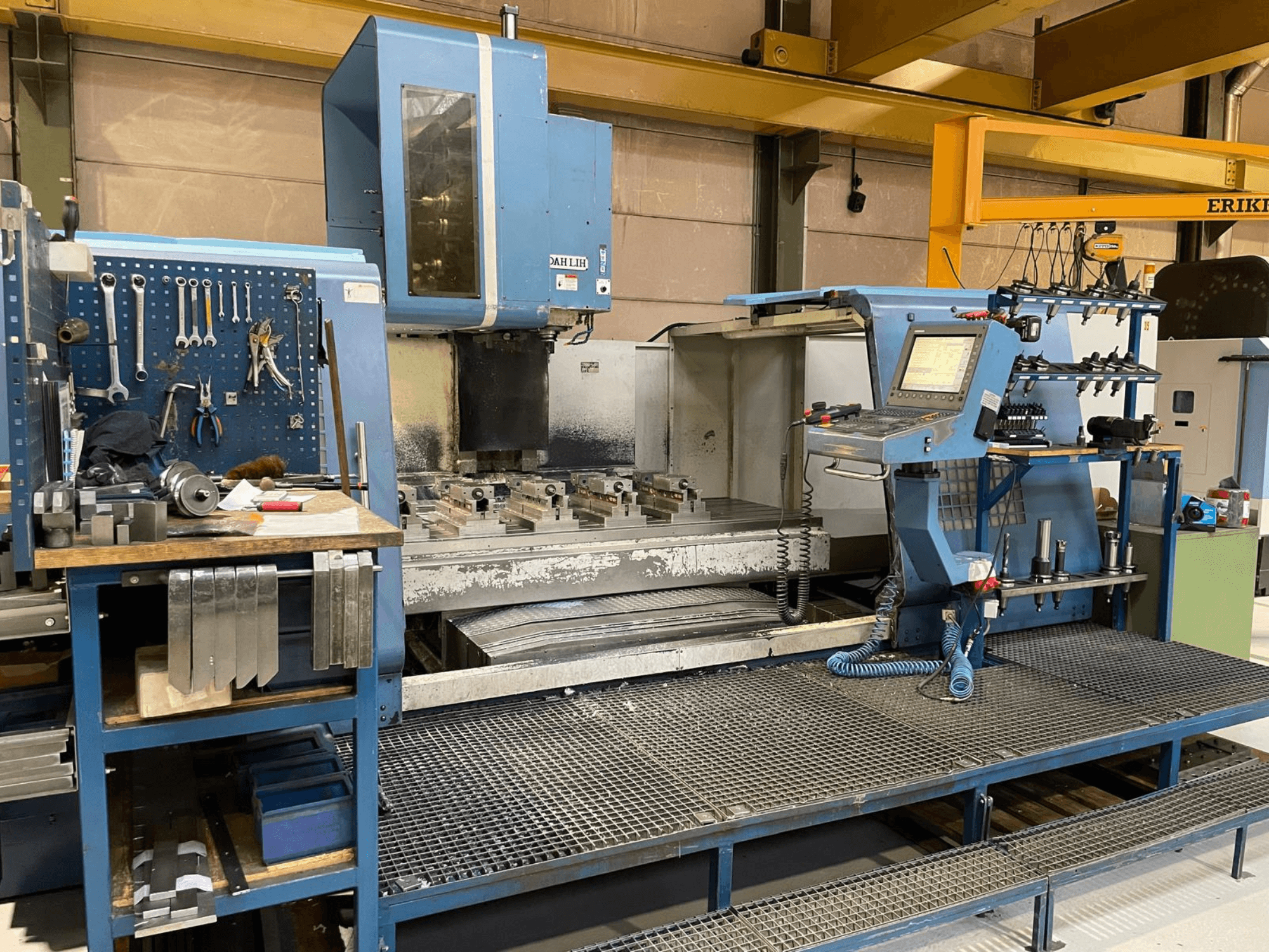 Vista frontal do centro de maquinação vertical DAH LIH MCV2600, mostrando o painel de controlo, a mesa de trabalho e a área de armazenamento de ferramentas.