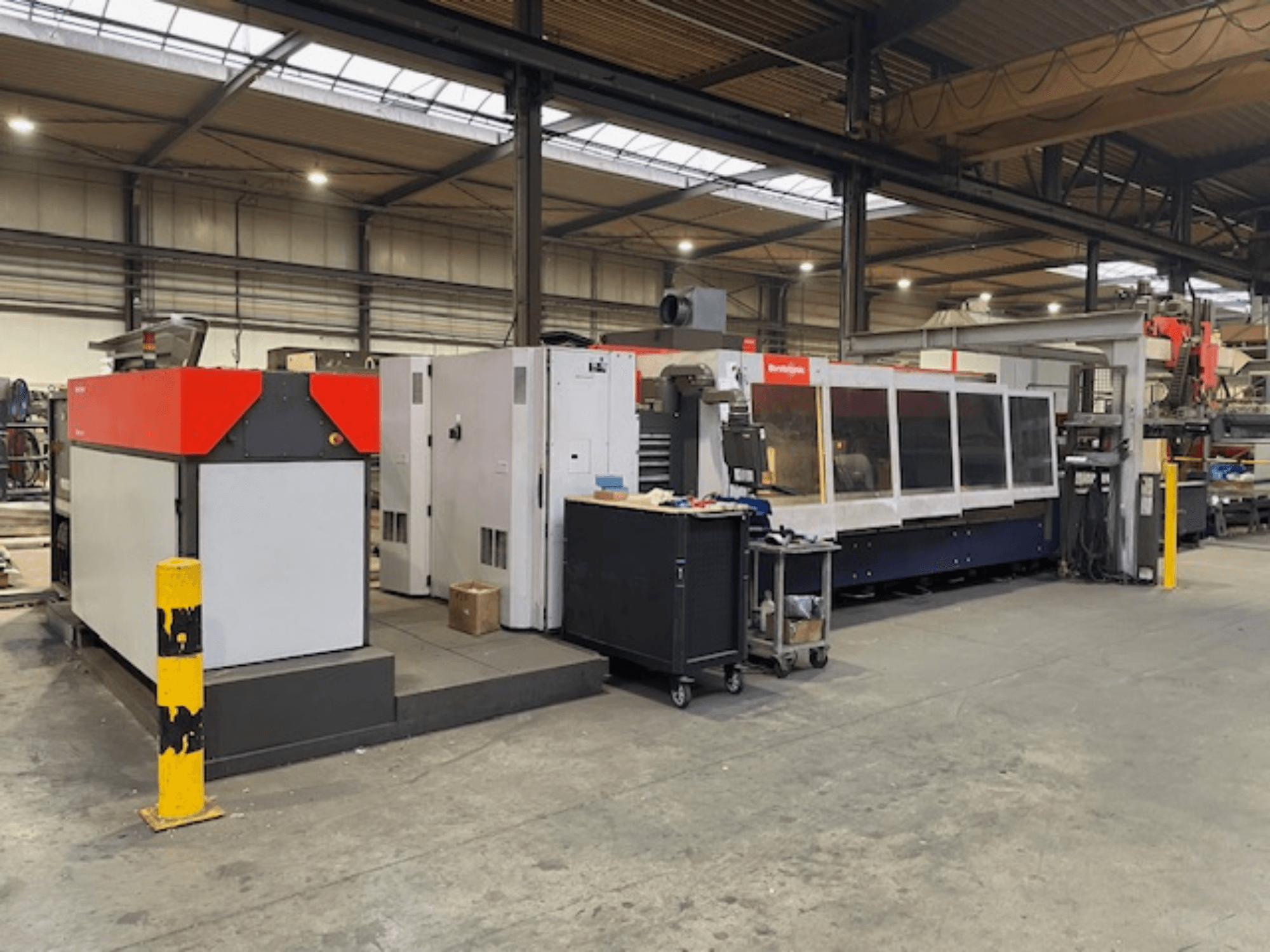 Máquina de corte a laser CO2 BySpeed 3015 da Bystronic, vista lateral numa oficina, com elementos de design distintos em vermelho e cinzento.