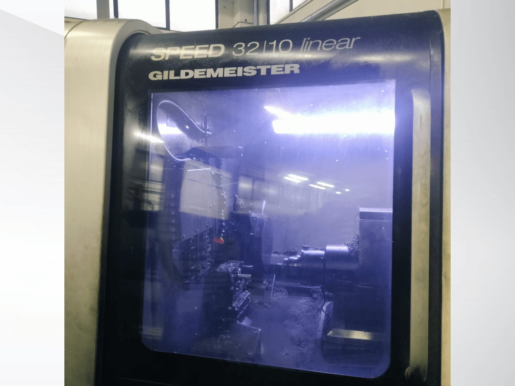 Vista frontal da máquina CNC linear Gildemeister SPEED 3210, mostrando os componentes internos e o líquido de refrigeração em funcionamento.