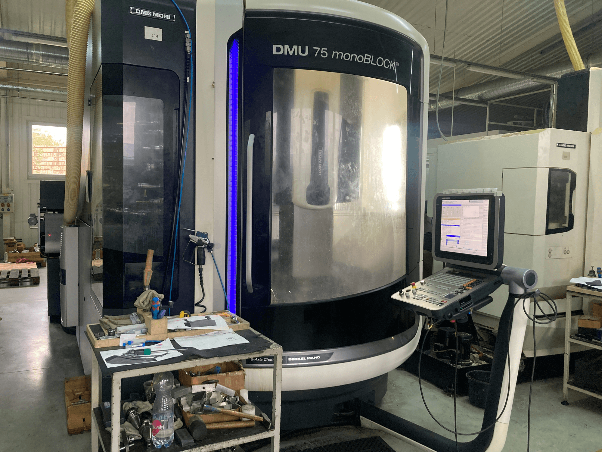 Máquina CNC DMG MORI DMU 75 monoBLOCK®, vista frontal, com painel de controlo, ferramentas e uma área de trabalho com materiais.