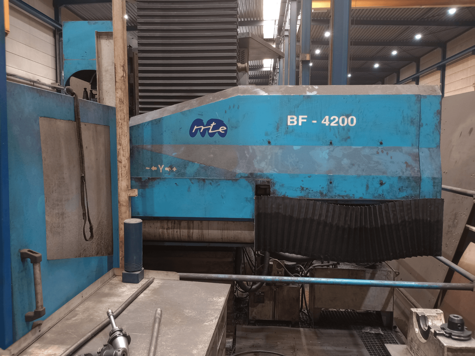 Fresadora de bancada MTE BF 4200, vista lateral, mostrando o exterior azul e os componentes detalhados da máquina num ambiente de oficina.