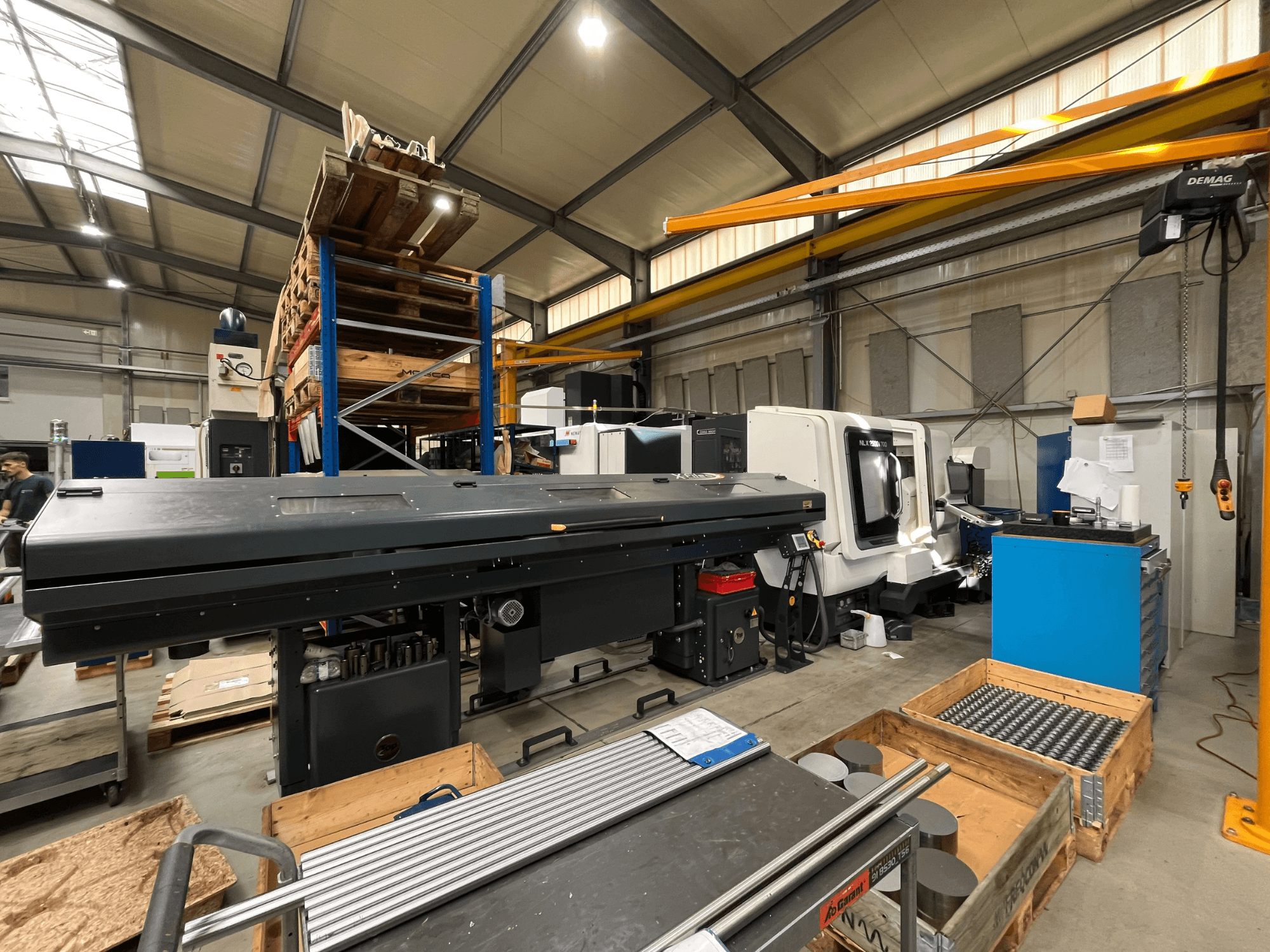 Torno horizontal DMG MORI MORI NLX 2500/700 SY numa oficina, visto de lado, com a área de armazenamento e as ferramentas em segundo plano.