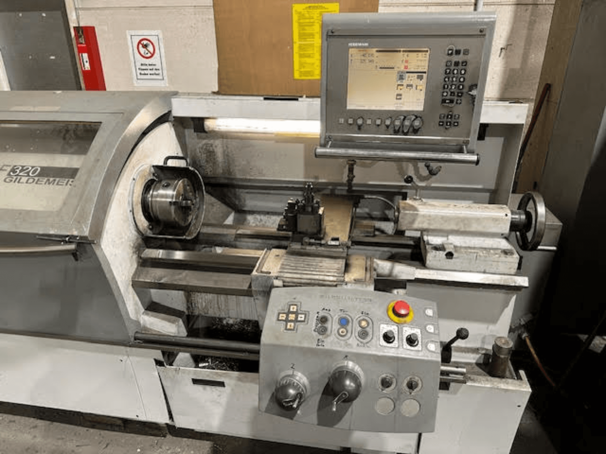 Torno horizontal HERMLE NEF 320, vista frontal que mostra o painel de controlo, a área de ferramentas e a configuração da peça metálica.