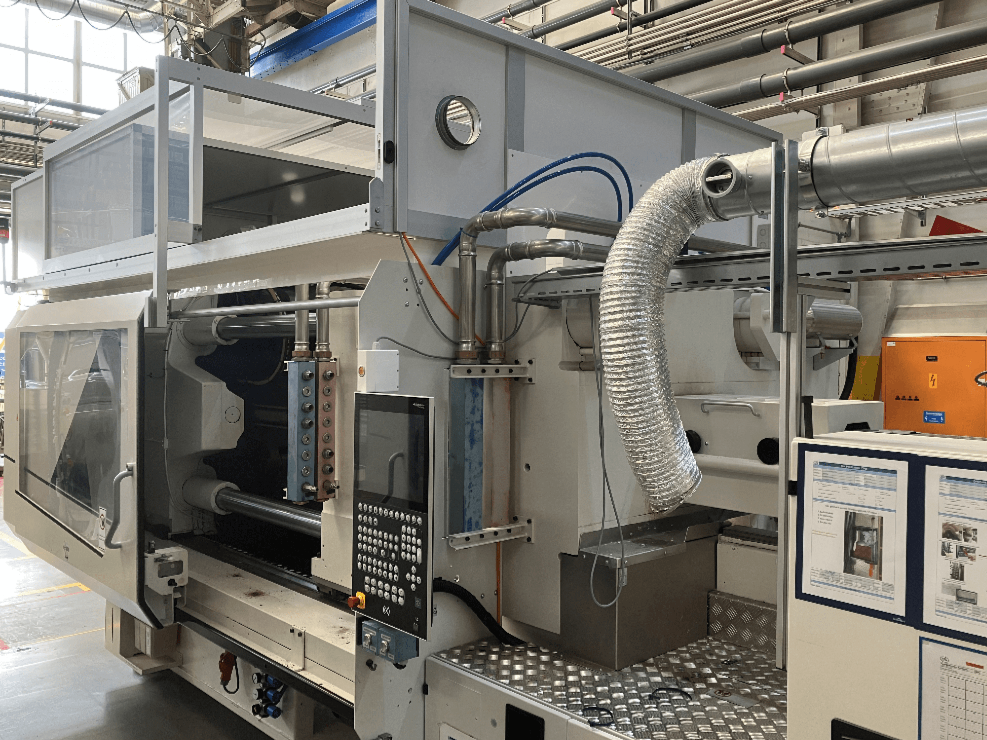 Máquina industrial da marca X, vista lateral mostrando o painel de controlo, condutas e componentes da máquina numa fábrica.