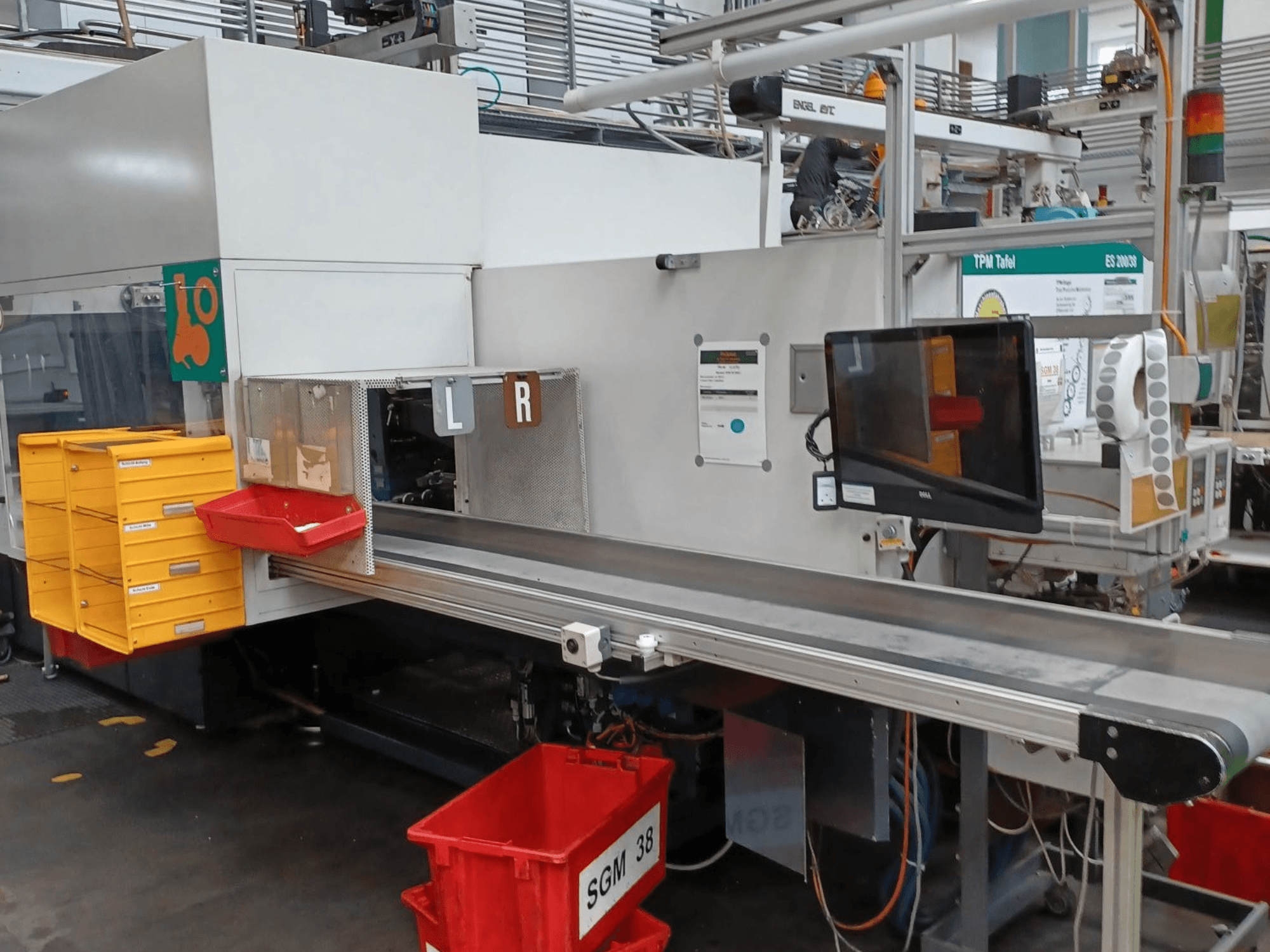 Máquina de triagem industrial com caixas amarelas e vermelhas, vista lateral, com um monitor de controlo e compartimentos etiquetados para triagem.