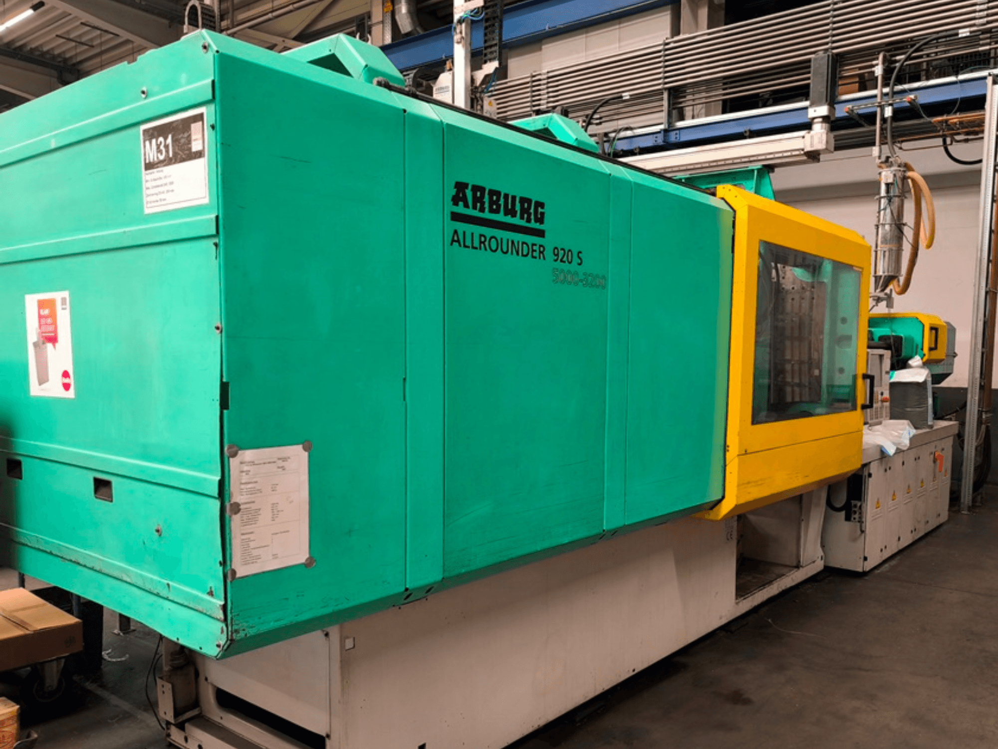 Máquina de moldagem por injeção Arburg Allrounder 920 S em azul água e amarelo, vista lateral mostrando o painel de controlo e os componentes.