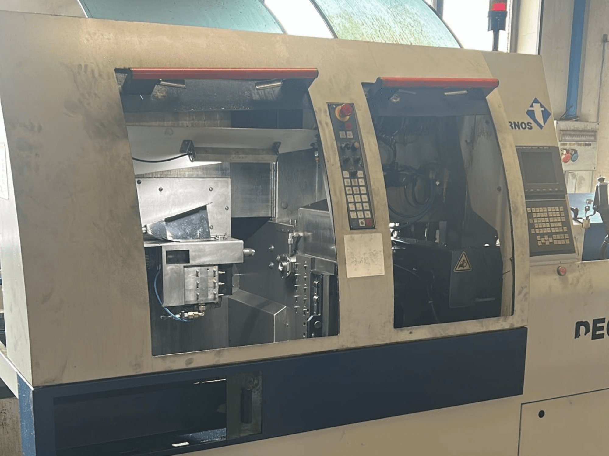 Texto alternativo: Vista frontal do torno de tipo suíço TORNOS Deco 13 b com painéis de controlo e componentes internos visíveis.
