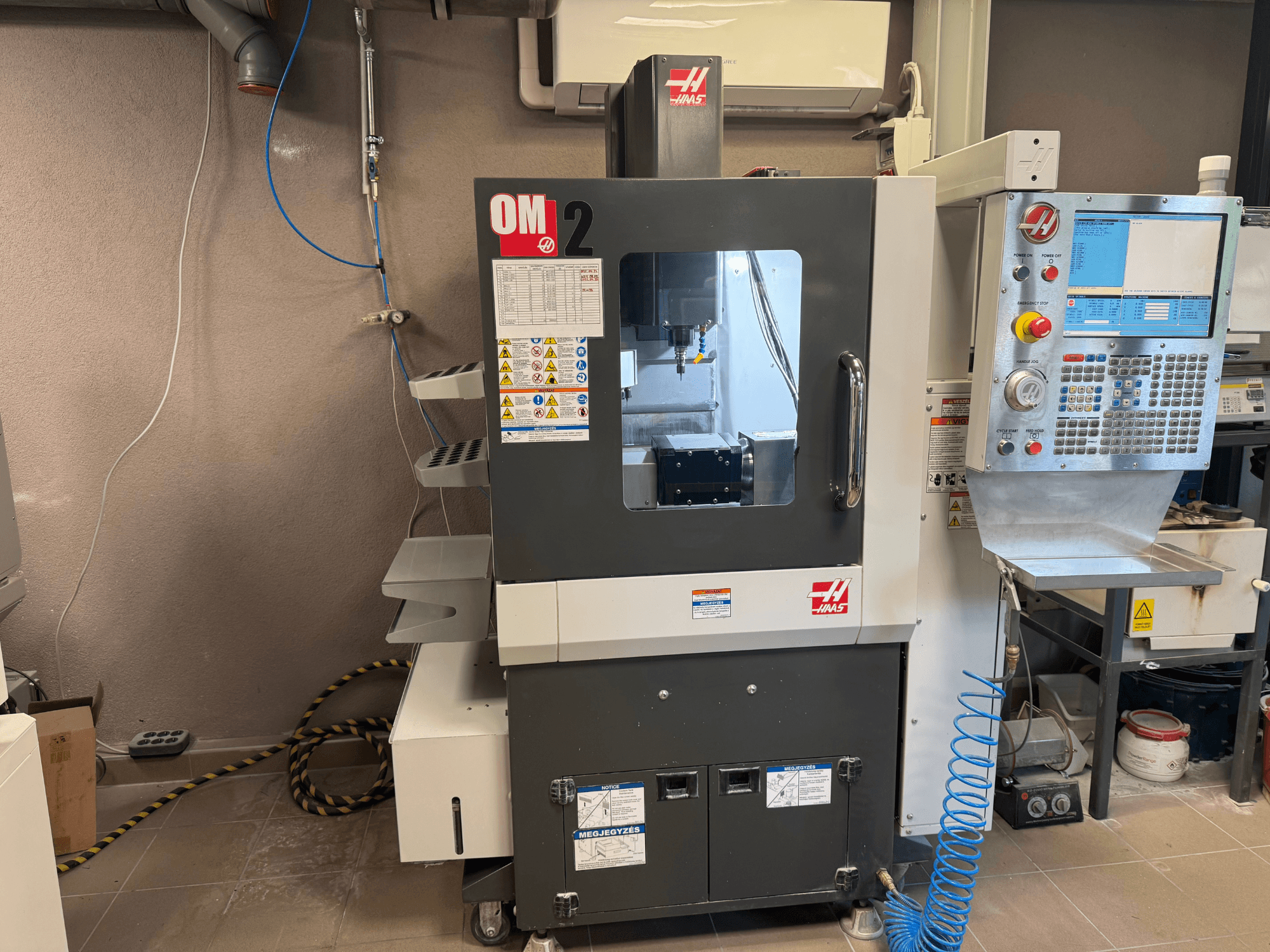Máquina CNC Haas OM-2, vista frontal, com painel de controlo, spindle e etiquetas de segurança, colocada num ambiente de oficina.