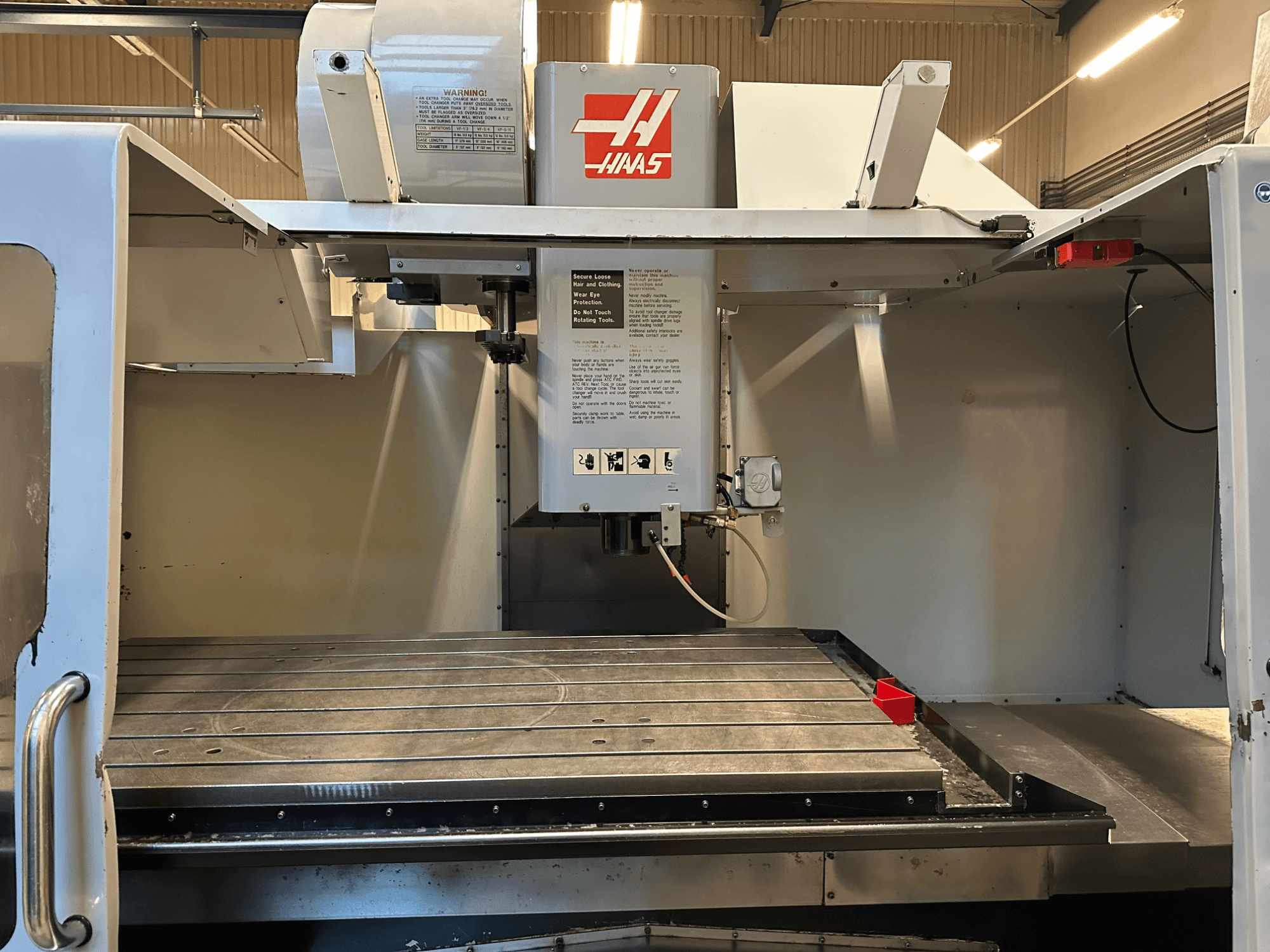 Fresadora CNC Haas, modelo VF-2, vista frontal mostrando controlos, mesa de trabalho em metal e etiqueta de segurança no painel.