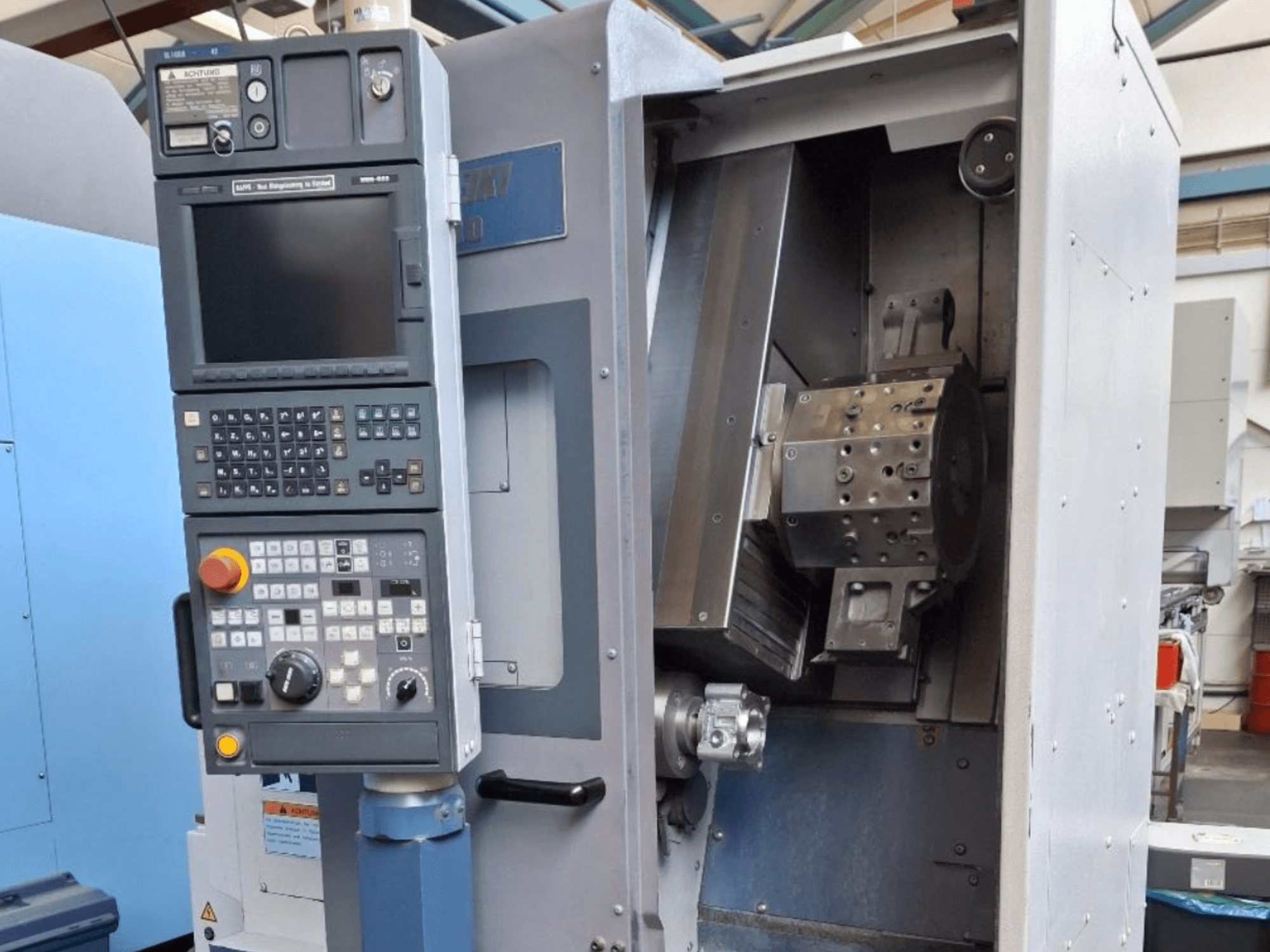 Vista frontal do torneiro horizontal MORI SEIKI SL 1000, com painel de controlo e mecanismo interno detalhado.