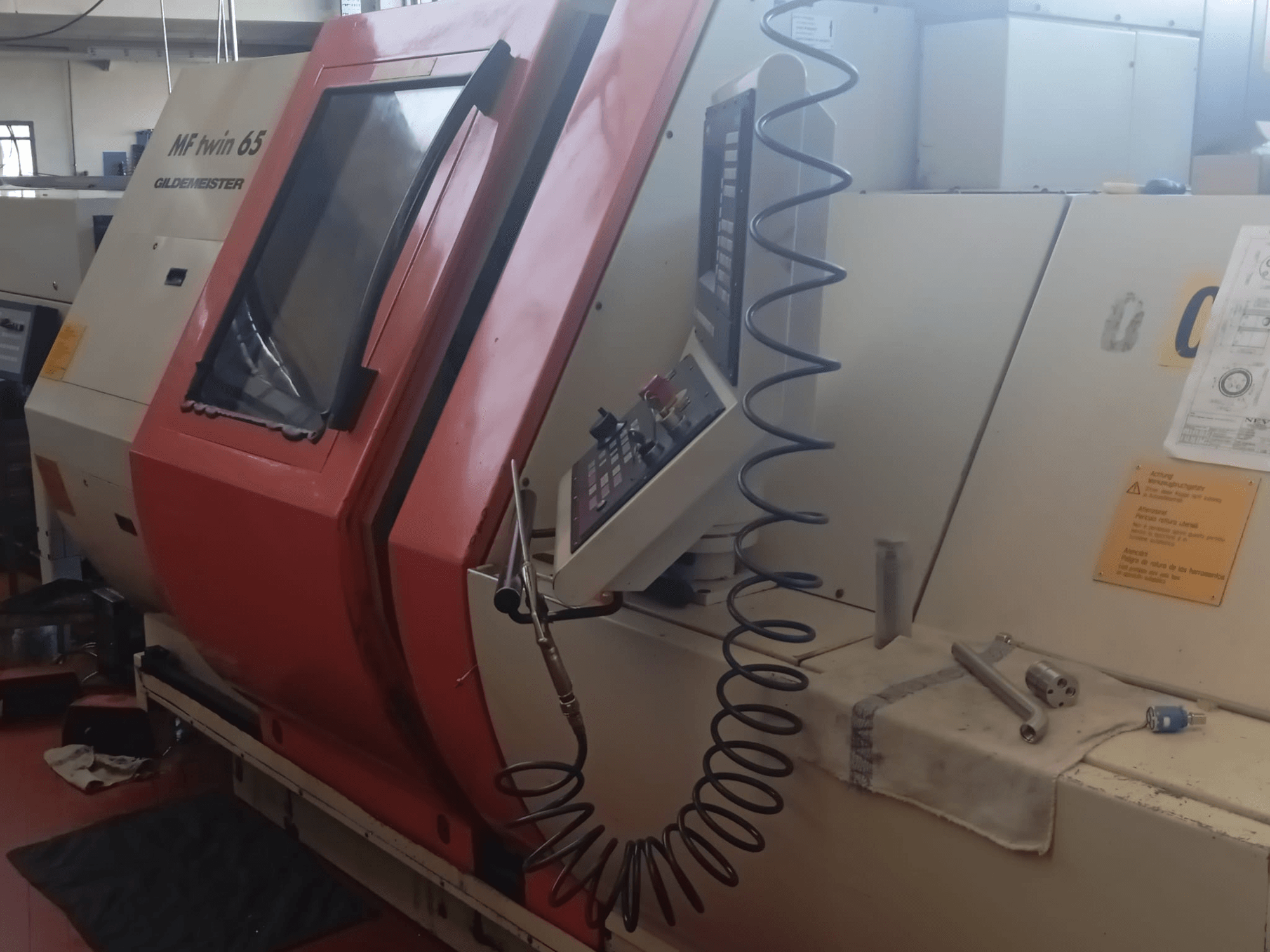 Máquina MF twin 65 Gliedemeister laranja e branca, vista frontal, com painel de controlo e ferramentas sobre um pano.