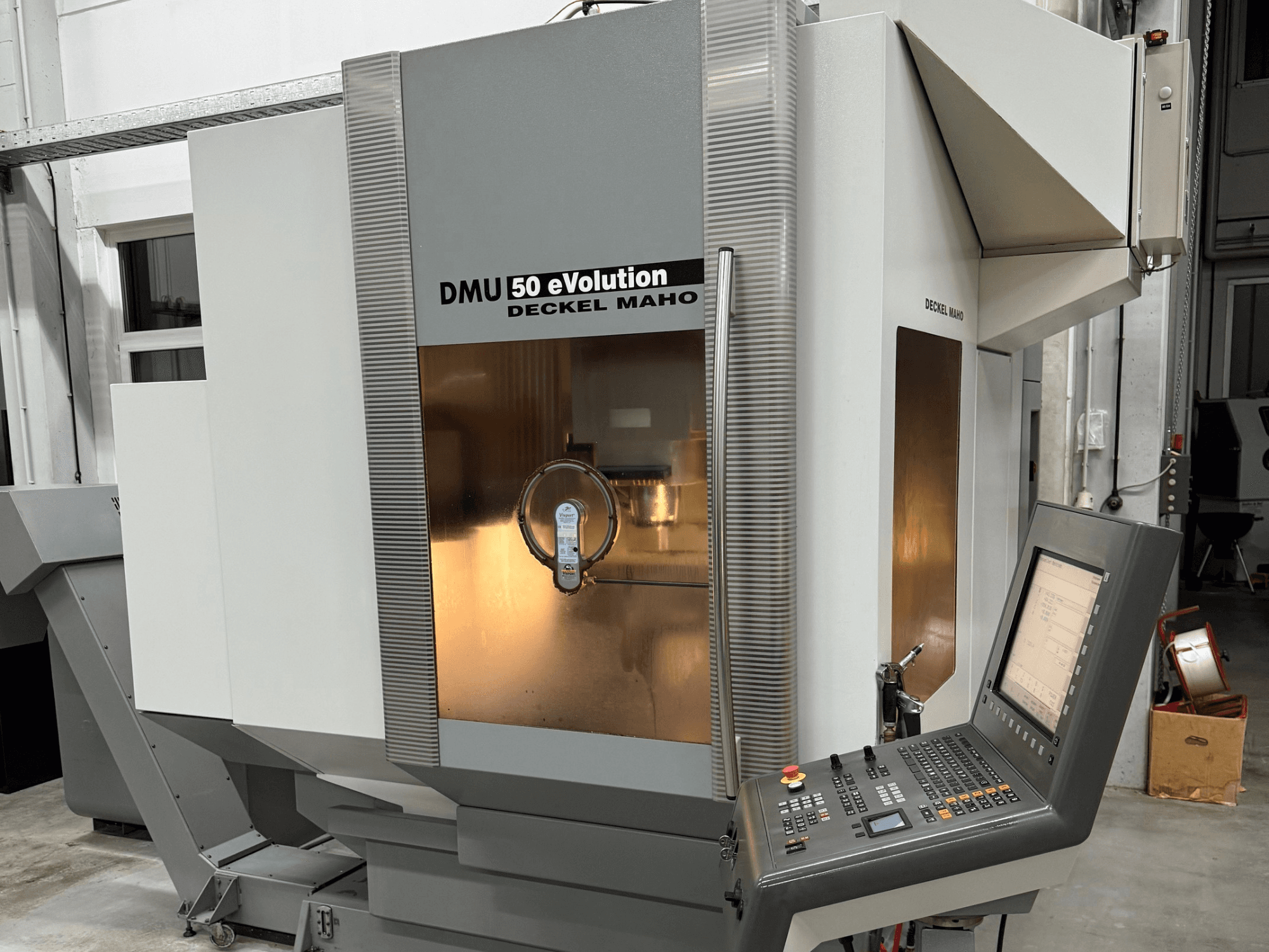 DMU 50 eVOLUTION de Deckel Maho, vista frontal de uma fresadora CNC com painel de controlo, superfície brilhante e porta-ferramentas visível.
