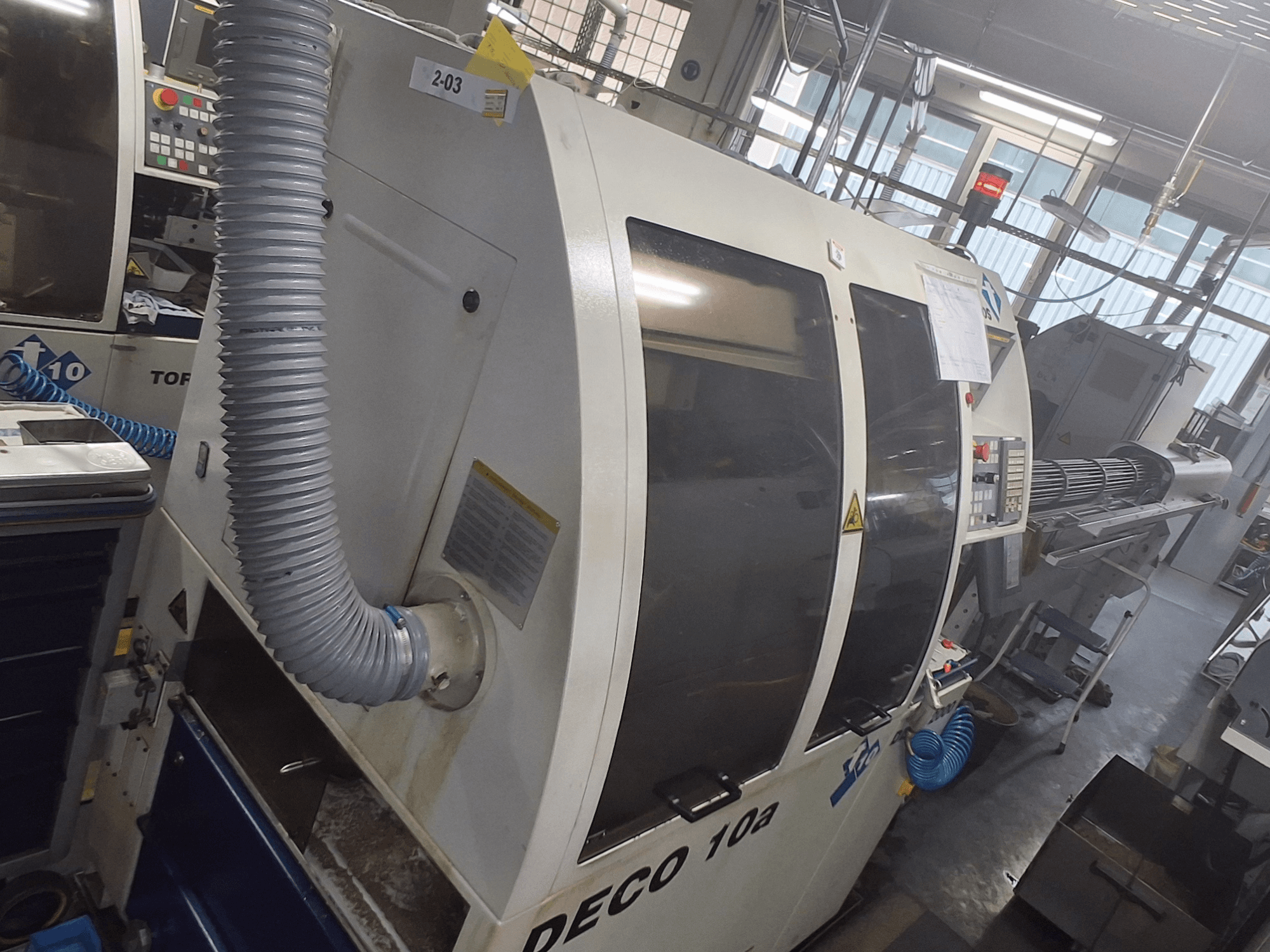 Máquina DECO 10a em vista frontal; apresenta um grande painel de controlo, condutas e autocolantes operacionais visíveis.