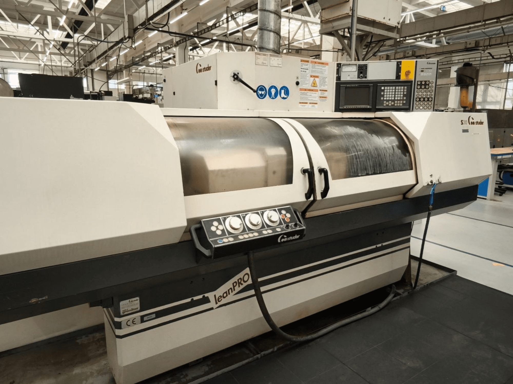 STUDER S30 LEAN PRO, retificadora cilíndrica, vista lateral, mostrando o painel de controlo e a cobertura do rebolo num ambiente industrial.