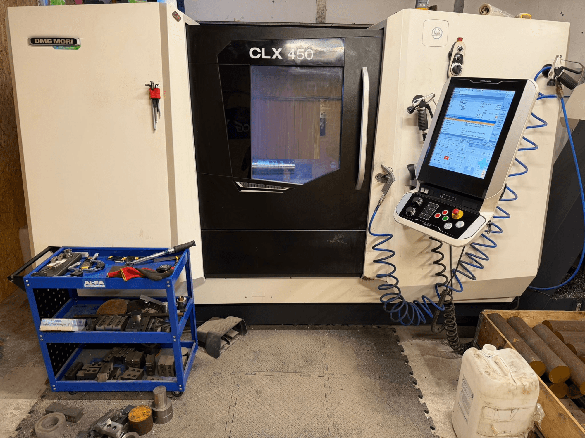 Vista frontal do torno horizontal DMG MORI CLX 450 V3, com painel de controlo e carrinho de ferramentas próximo com equipamento.