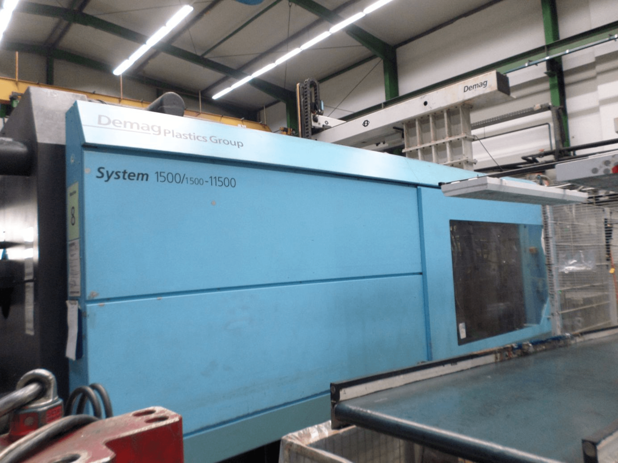Máquina de moldagem por injeção hidráulica Demag D 650, na cor azul; vista lateral que mostra a etiqueta «System 1500/1500-11500» e a área de operação.