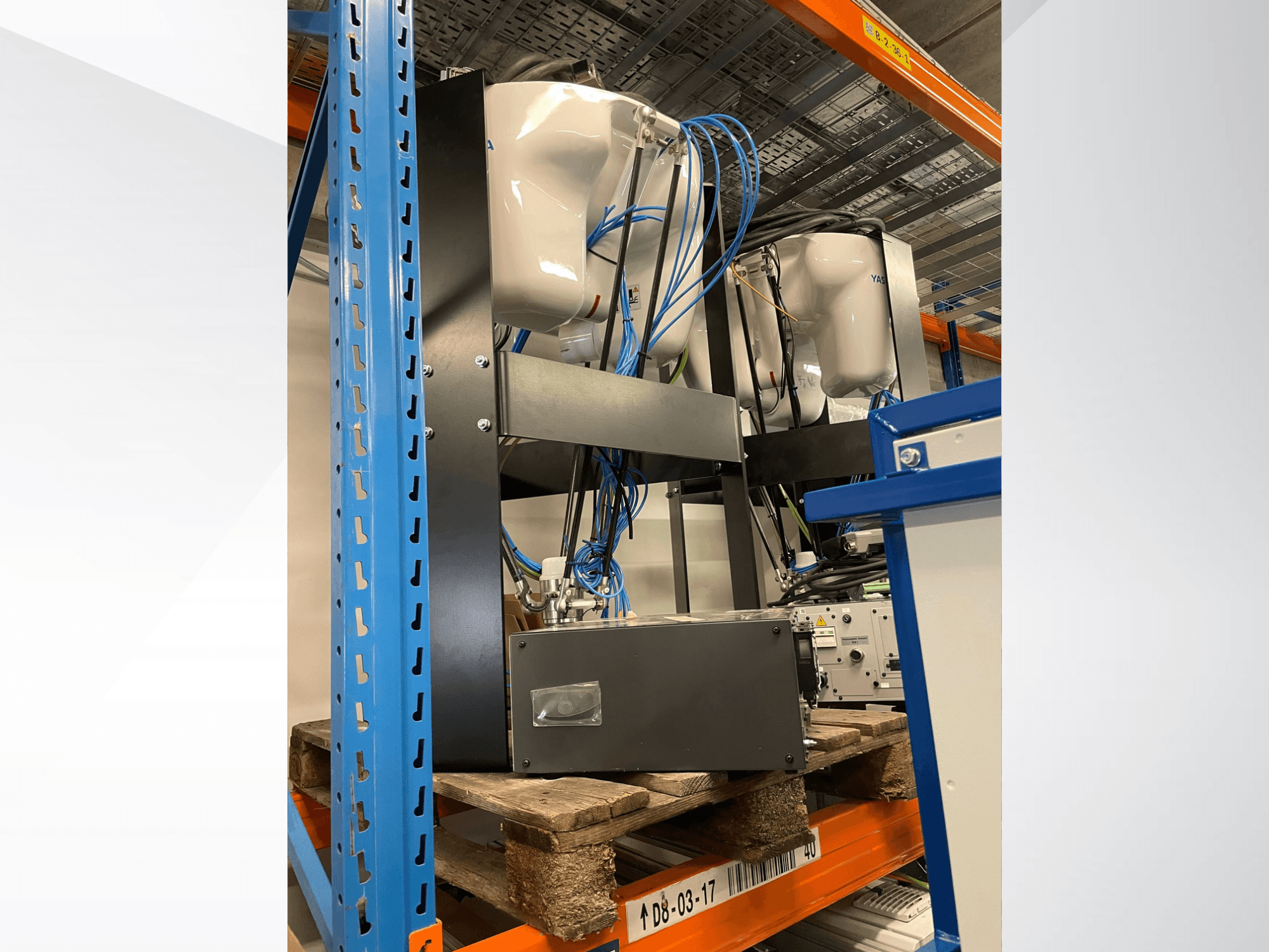 Braço robótico Yaskawa Motoman MPP3H, visto de lado, com a cablagem e os componentes visíveis numa prateleira de armazenamento.