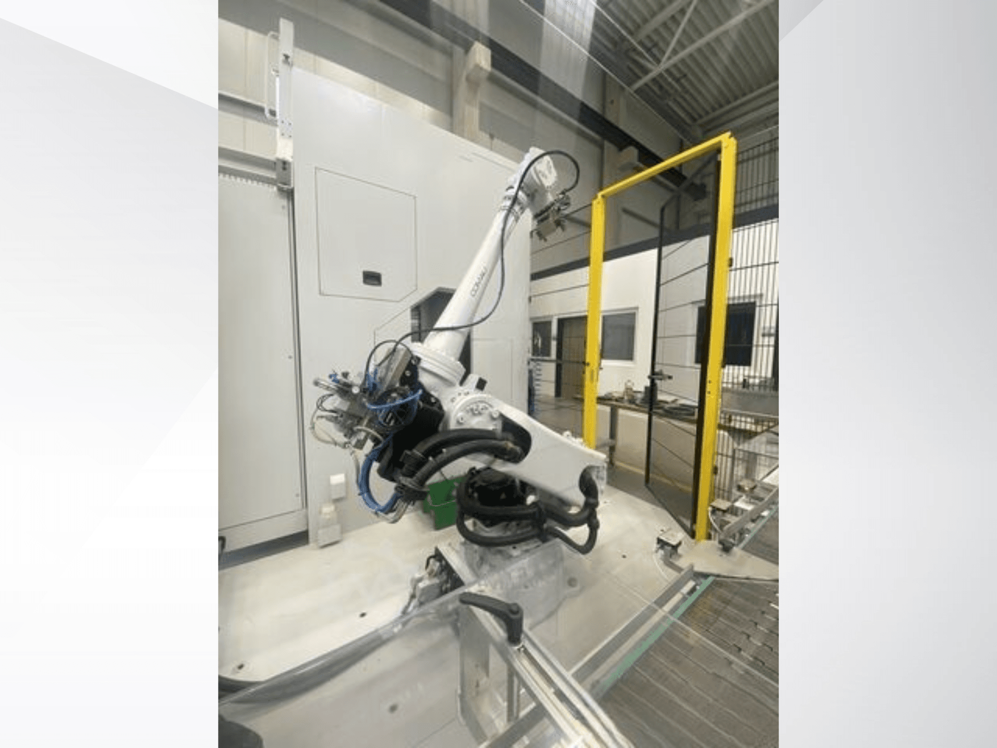 Braço robótico COMAU Smart NJ 40-2.5 em vista lateral, com cabos e uma porta de segurança amarela numa configuração de fábrica.