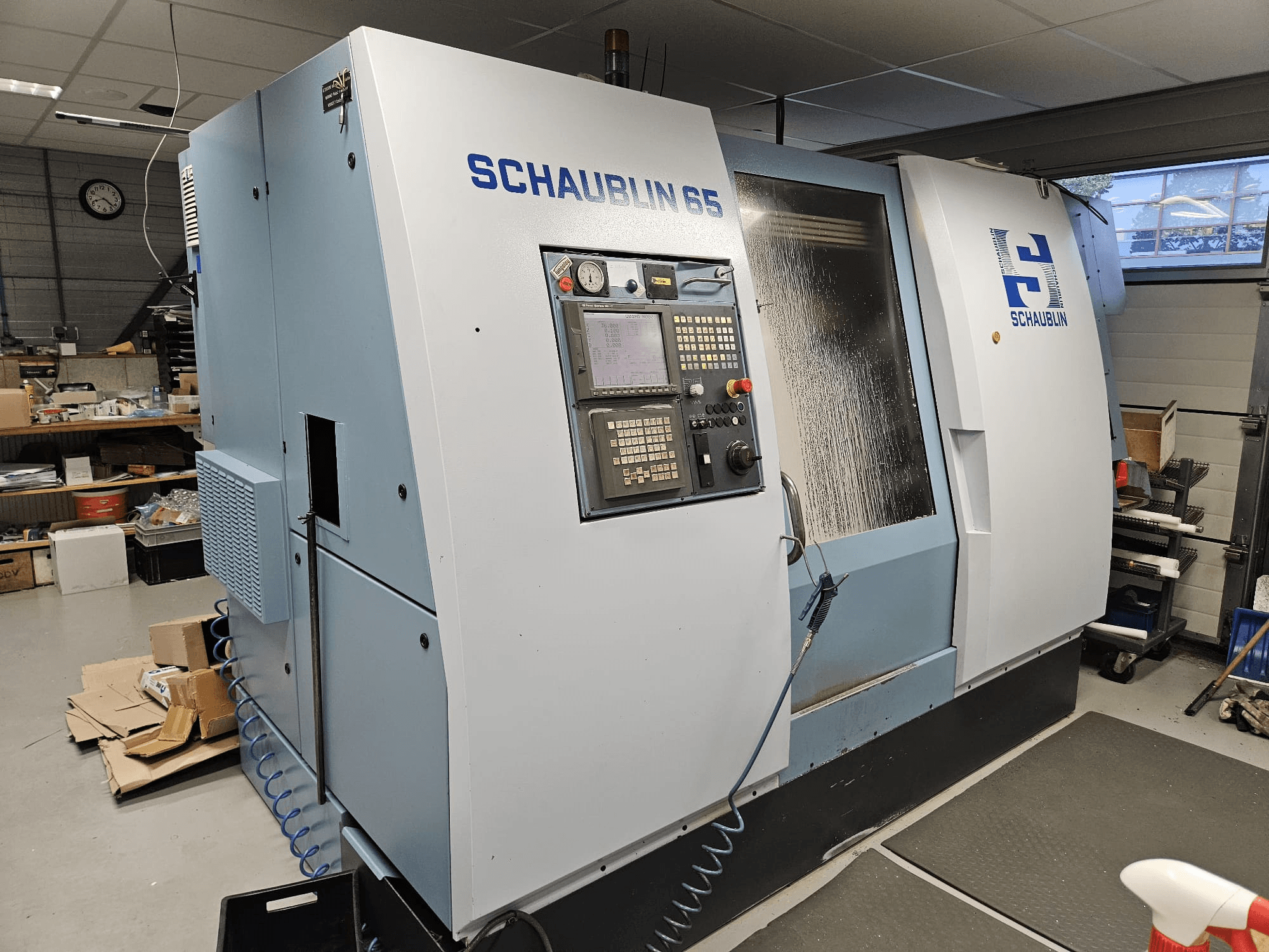 Máquina CNC SCHAUBLIN 65, vista lateral, com painel de controlo, caixa azul e cinzenta e sistema de refrigeração visível.