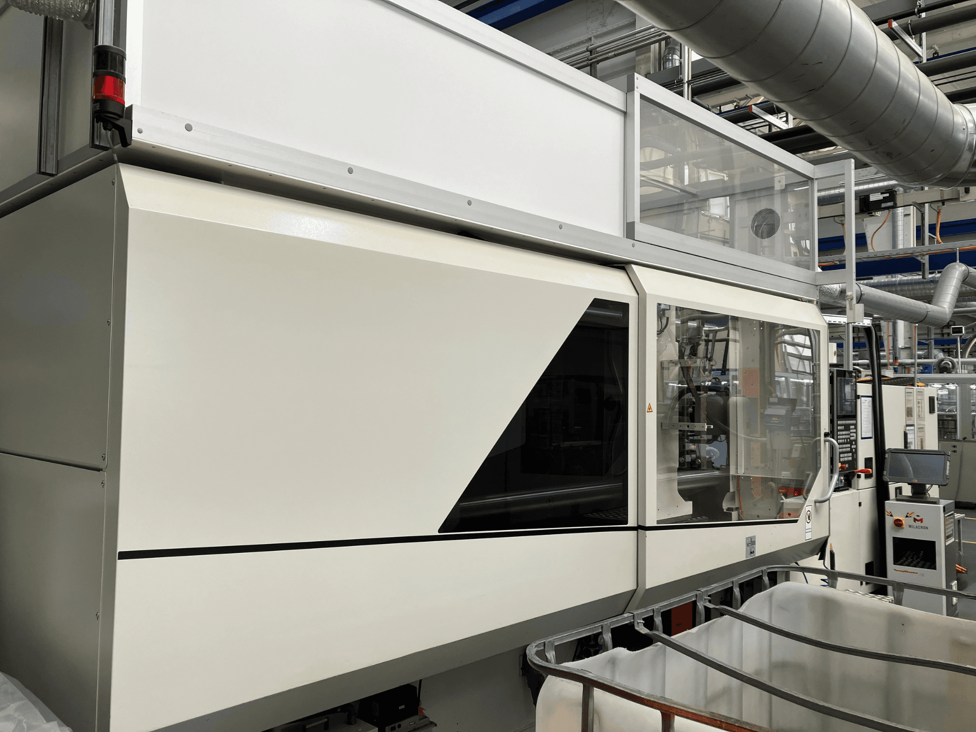 Vista frontal da máquina industrial, com um design branco elegante, painel de visualização e secção de vidro para visibilidade dos componentes.