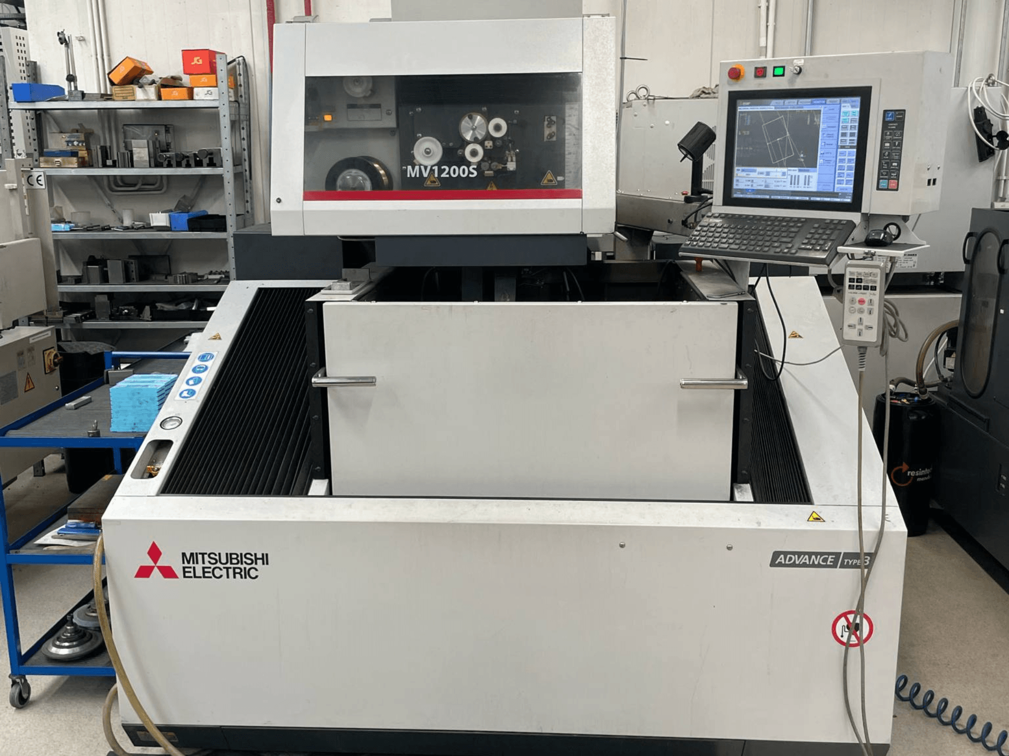 Máquina de eletroerosão por fio Mitsubishi MV1200S vista de frente, apresentando o painel de controlo e a área de trabalho, com avisos de segurança visíveis.
