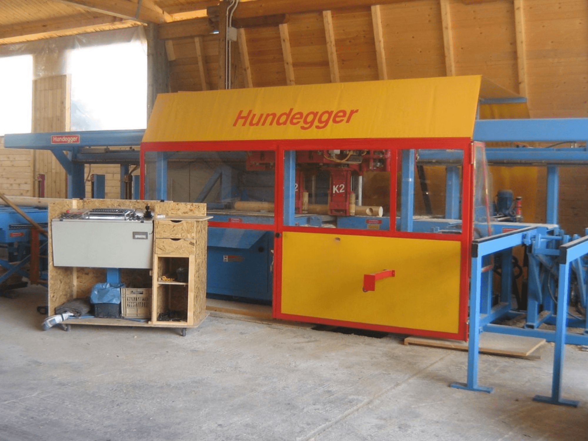 Centro de maquinação CNC para madeira HUNDEGGER K2 4 assi numa oficina, vista frontal mostrando o desenho amarelo e azul com mesa de trabalho.