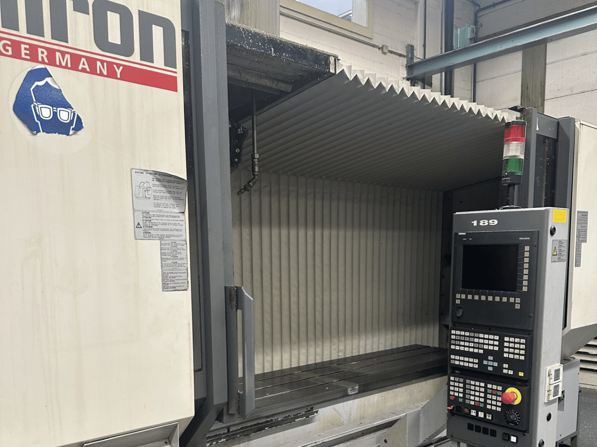 Texto alternativo: Vista frontal de uma máquina CNC Hermle com um painel de controlo com botões e um visor, com uma área de trabalho aberta.