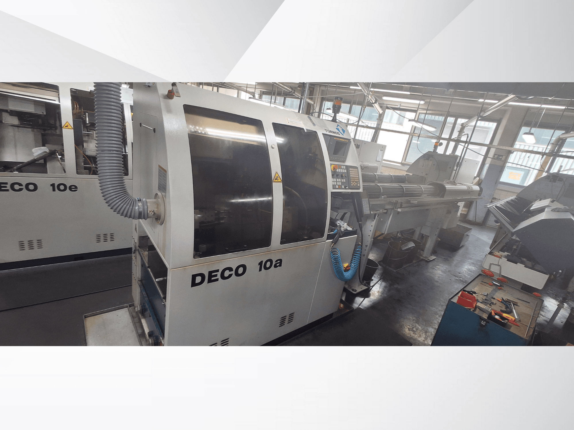 Máquina CNC DECO 10a numa oficina, mostrando a vista frontal, o painel de controlo e o sistema de escape. Apresenta uma construção robusta e ferramentas de precisão.