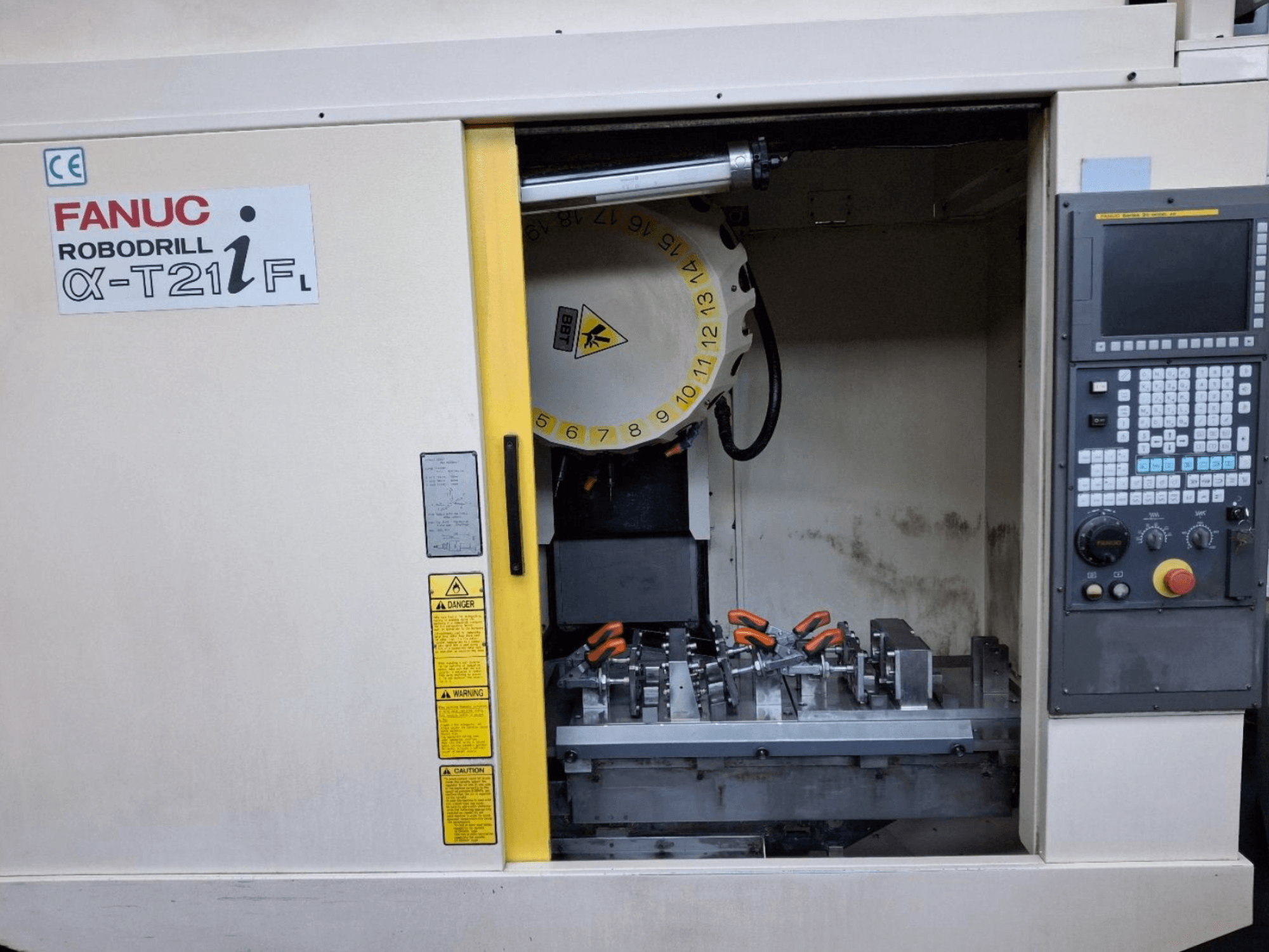 Vista frontal do centro de maquinação vertical FANUC ROBODRILL α-T21iFL, mostrando as ferramentas e os controlos no interior do armário da máquina.