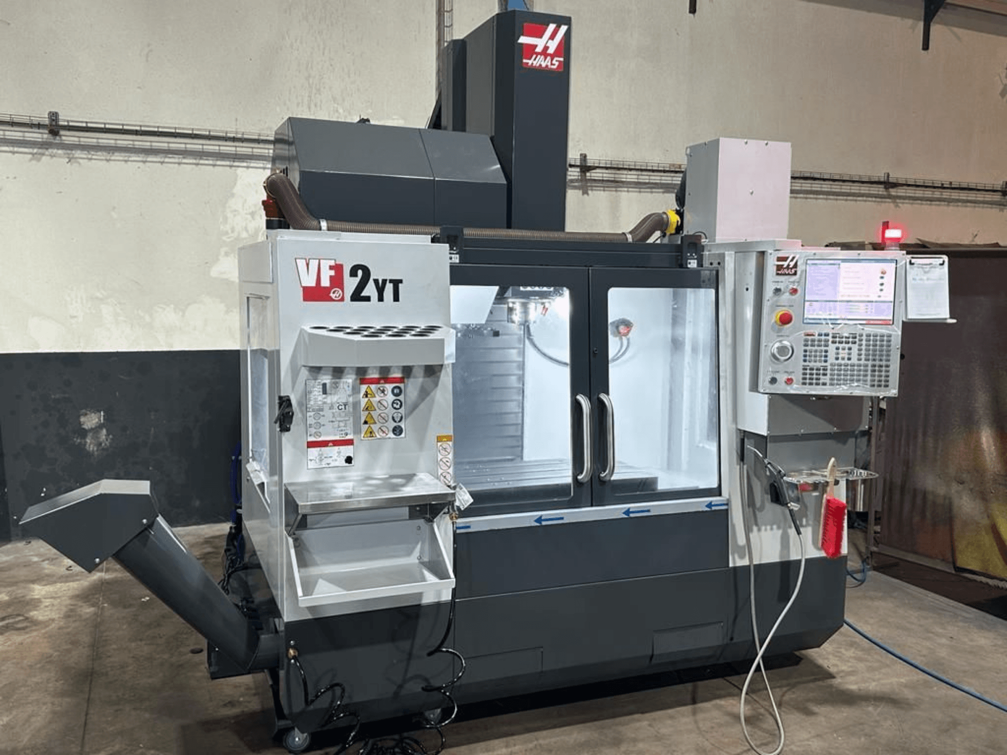 Centro de maquinagem vertical HAAS VF-2YT-EU, visto de frente, mostrando o painel de controlo e o compartimento de armazenamento de ferramentas.