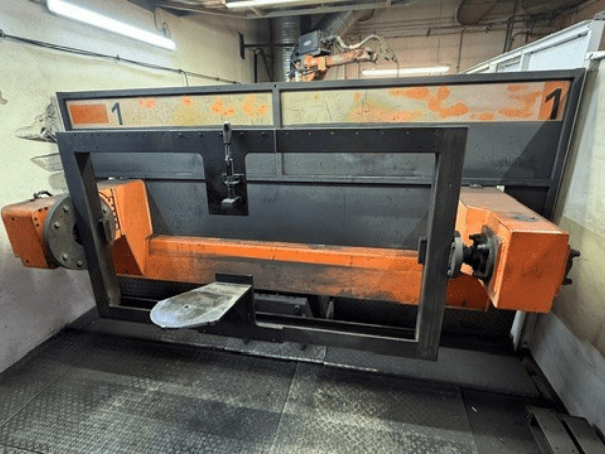 Vista frontal da célula de soldadura ABB IRB 2400L, mostrando uma grande estrutura robótica com componentes laranja e pretos num ambiente de oficina.