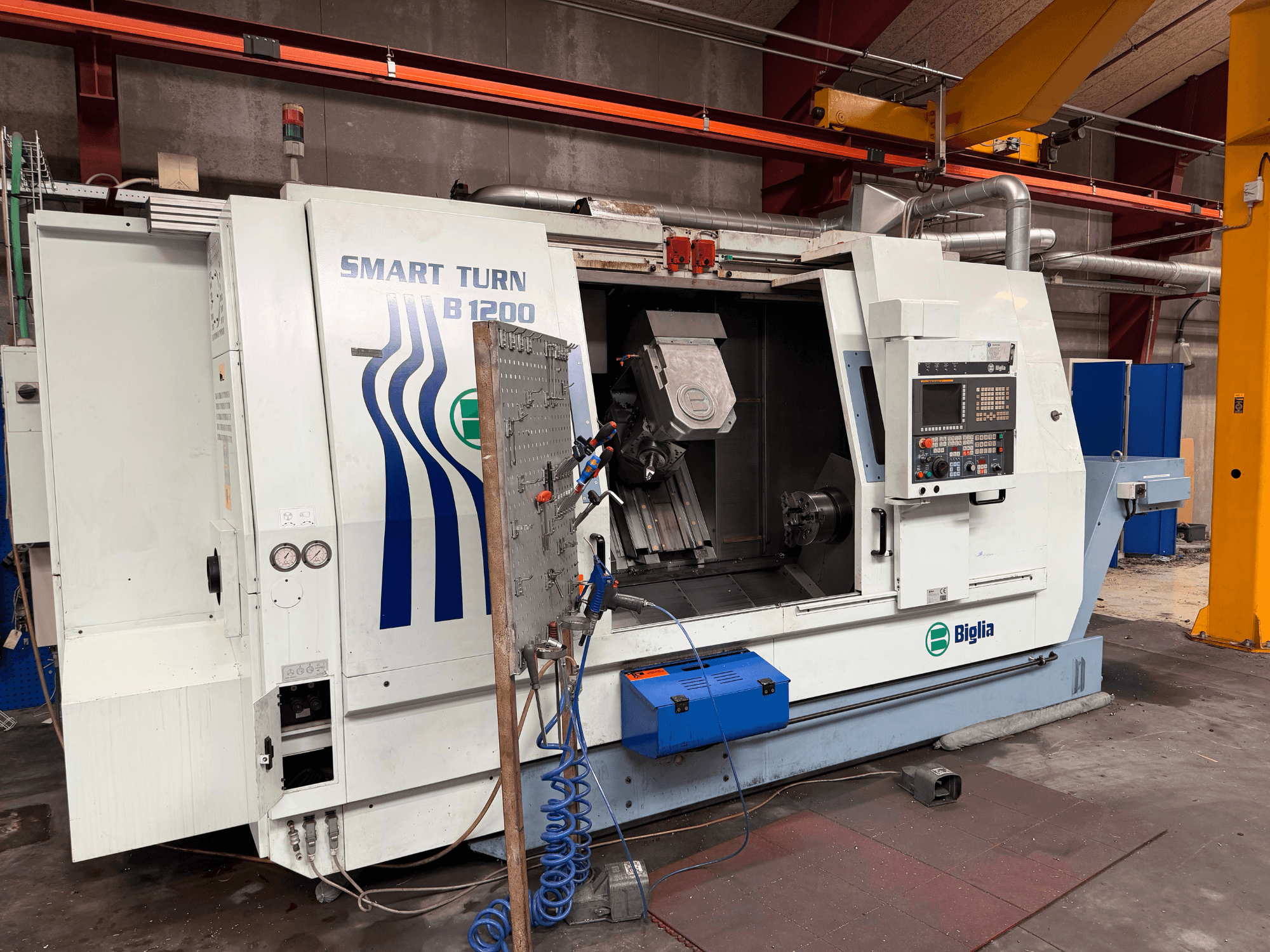 Centro de torneamento e fresagem Biglia B.1200/S-Smart, visto de frente; apresenta os comandos, uma peça no fuso e manómetros.