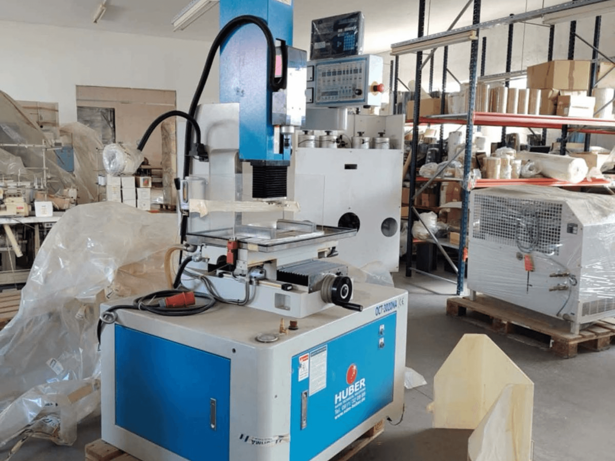 Máquina EDM para confeção de matrizes HUBER OCT-3020 NA numa oficina, vista frontal mostrando a caixa azul e cinzenta, os controlos digitais e a área de trabalho.