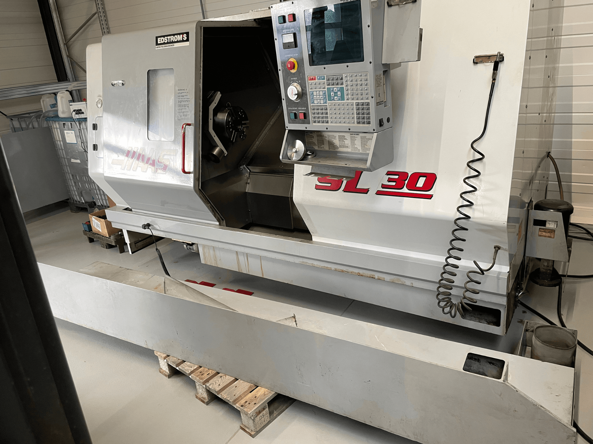 Torno CNC Haas SL 30 numa oficina, vista lateral, com painel de controlo e fuso aberto para tarefas de maquinação.