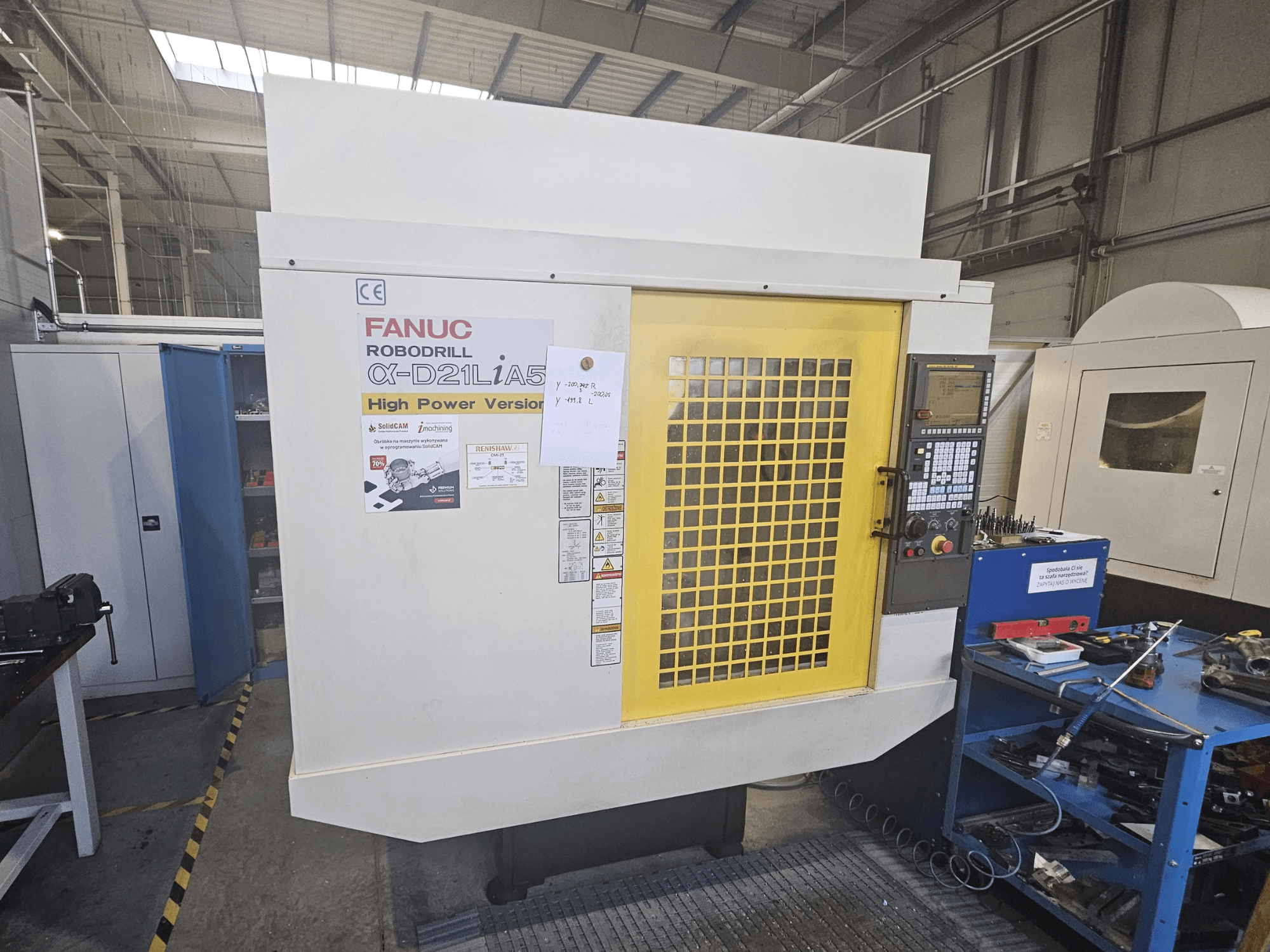 Vista frontal de um Robodrill α-D21LiA5 da FANUC com a porta de segurança amarela, o painel de controlo e as ferramentas do espaço de trabalho nas proximidades.