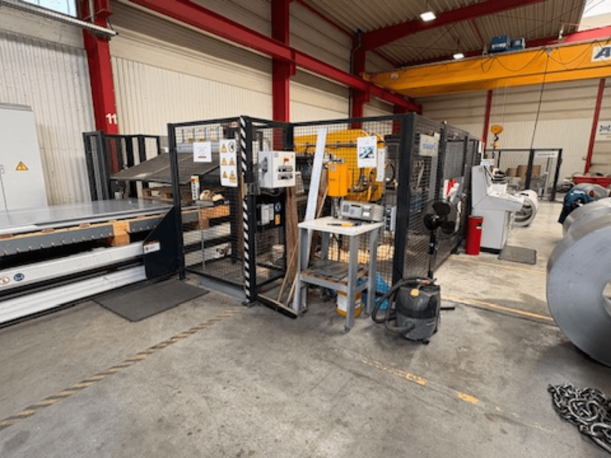 Máquina para chapas metálicas da SCHULER, modelo AC-PLS-1600-M, numa oficina; vista lateral que mostra a estrutura de proteção e o equipamento adjacente.