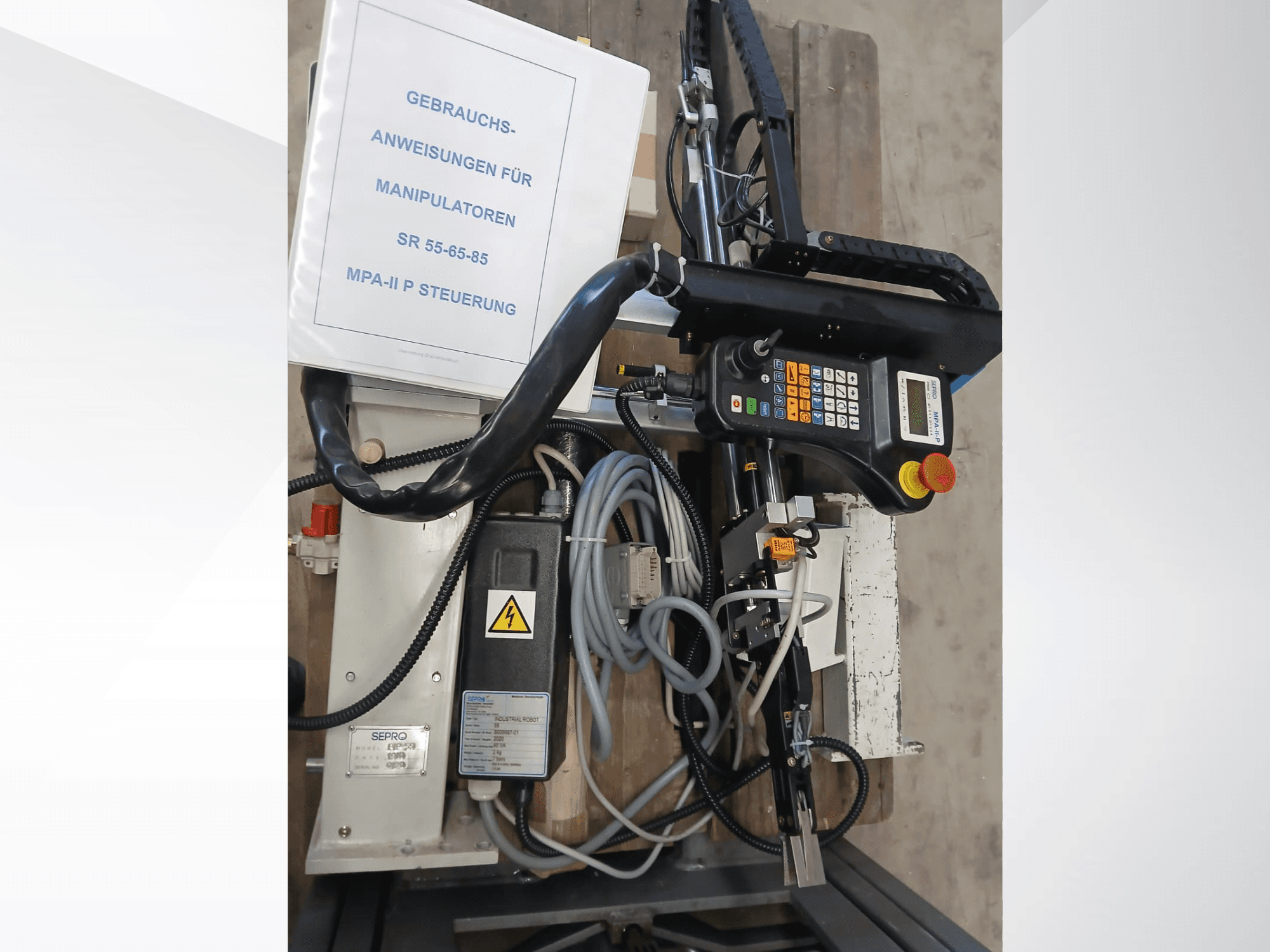 Painel de controlo e componentes do robô de pórtico Sepro PIP-55, visto de lado, com o manual do utilizador visível.