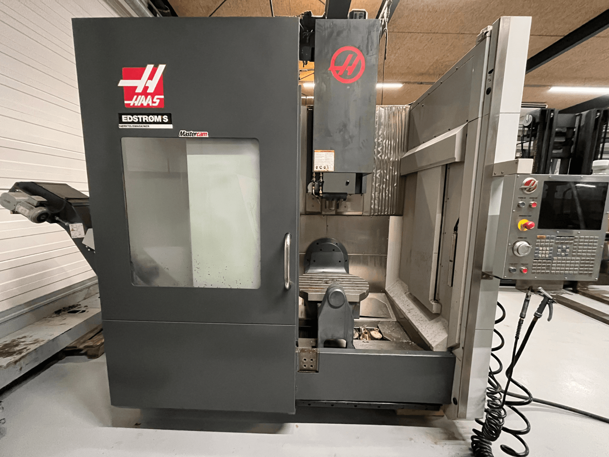 Vista frontal da máquina CNC Haas EDSTROM S mostrando o painel de controlo, a cabeça do spindle e a mesa de maquinação.