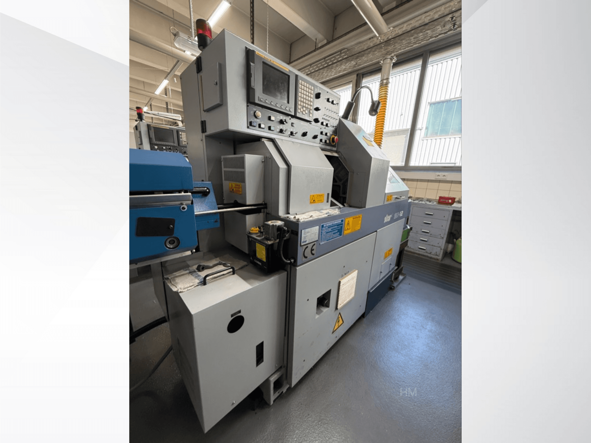 Vista frontal da máquina lithec 3231, mostrando o painel de controlo, o motor e a secção de alimentação azul num ambiente industrial bem iluminado.