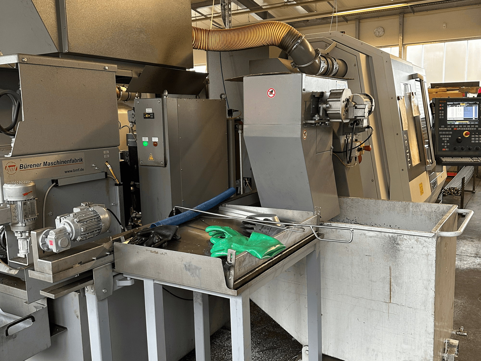 Torno de tipo suíço TRAUB TNL32-9, vista lateral, mostrando o painel de controlo, o motor e a área de corte com aparas de metal.