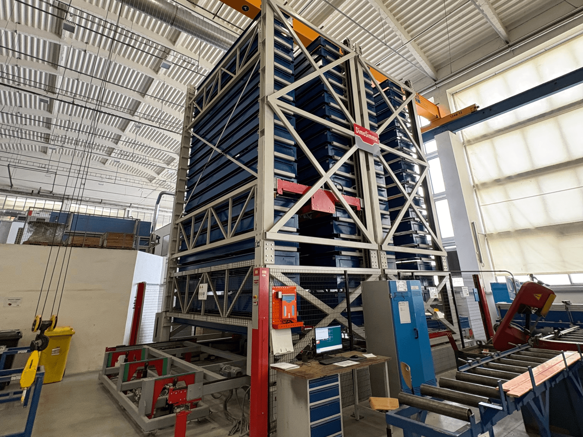 Máquina de chapa metálica DimaSimma EMS-30 TWIN numa oficina, vista frontal com tabuleiros azuis empilhados e estação de controlo visível.