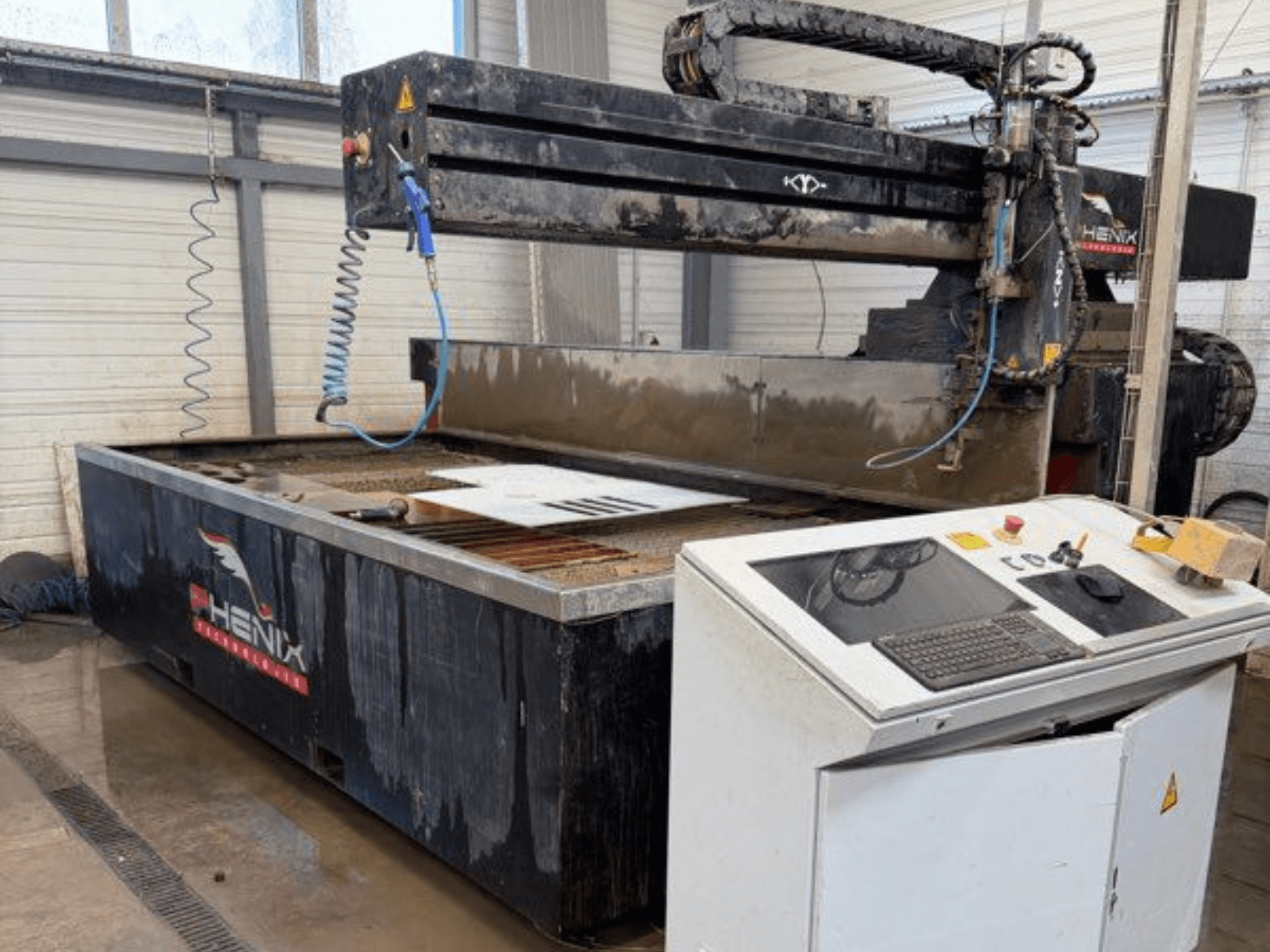 Máquina de corte por jato de água PHENIX MD JET 1530, vista frontal mostrando o painel de controlo e a área de corte com o depósito de água visível.