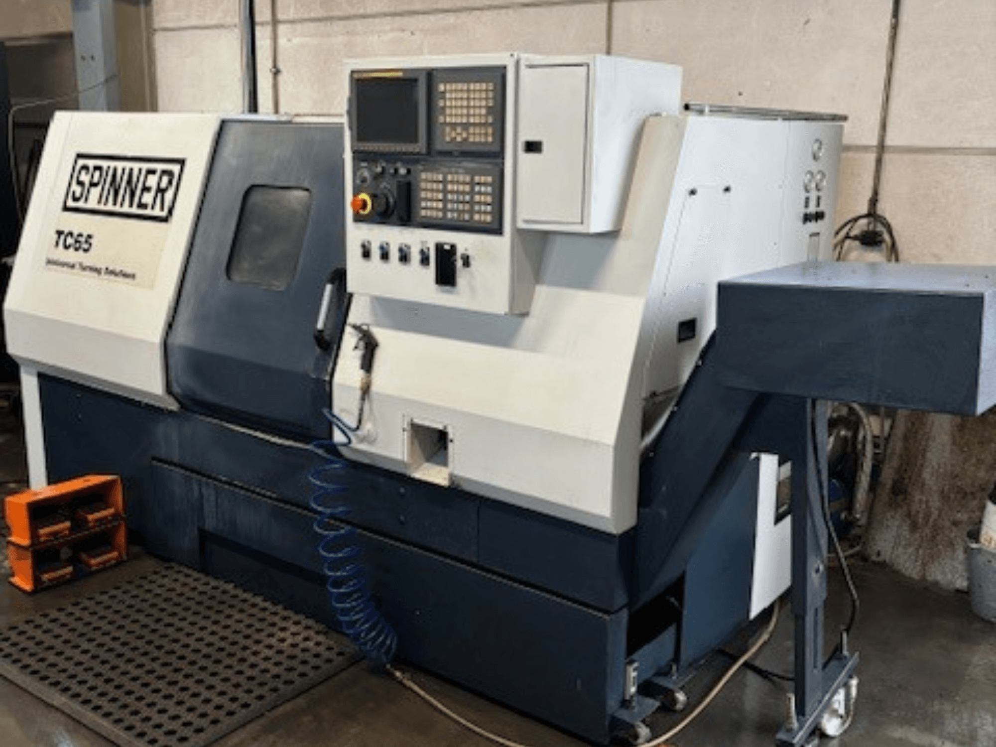 Torneiro industrial Spinner TC65, vista frontal, com painel de controlo, linha de ar comprimido e área de armazenamento de ferramentas.
