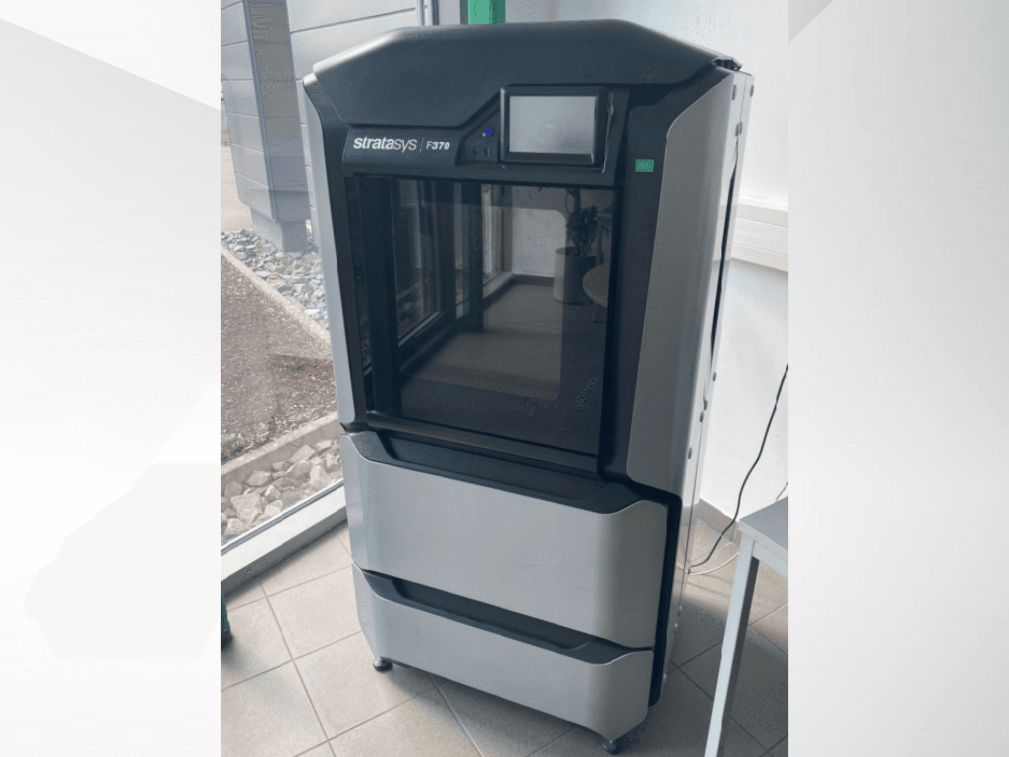 Impressora 3D de plástico Stratasys F370, vista frontal, apresentando um design elegante em preto e cinzento com um ecrã tátil.