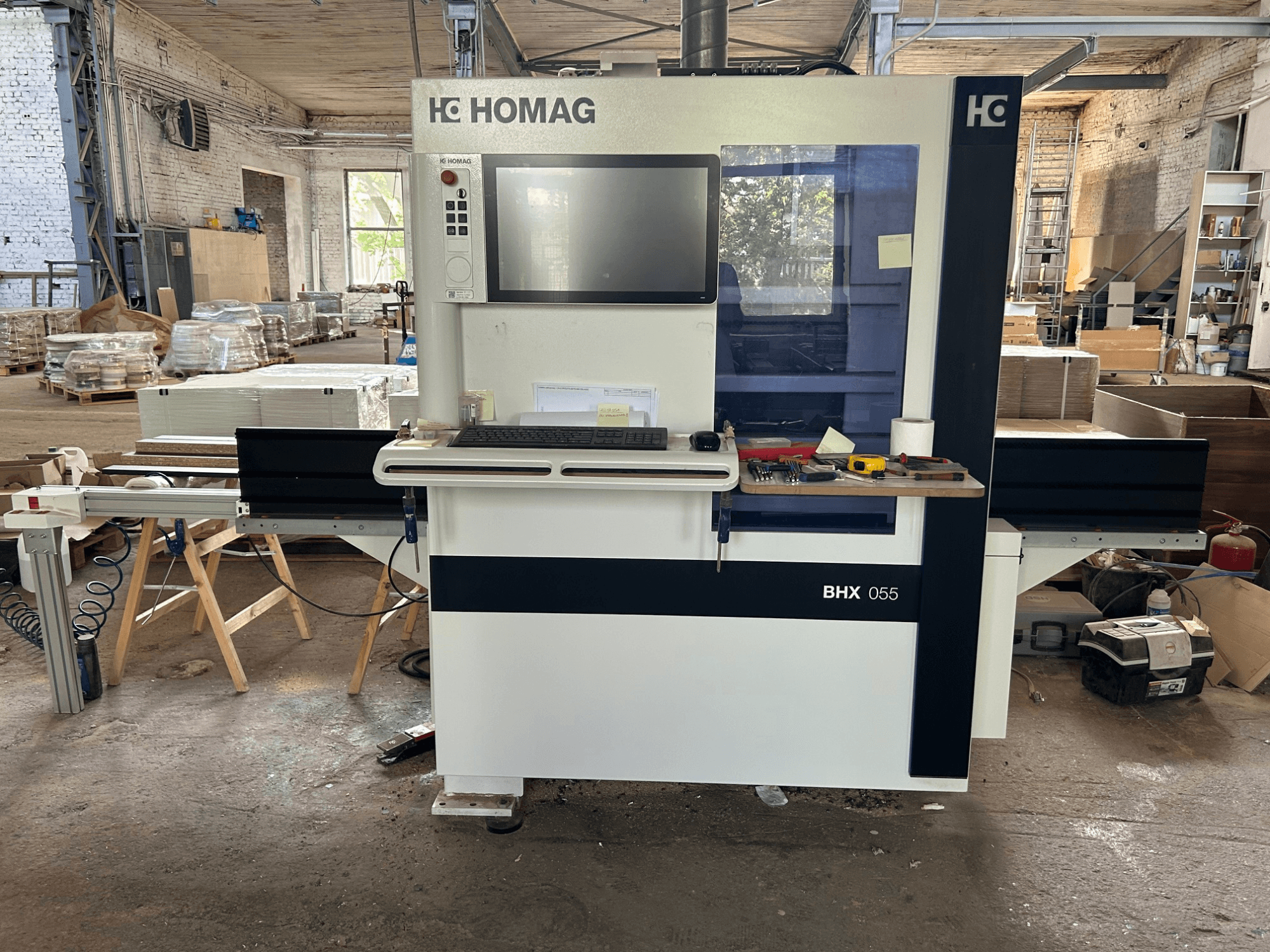 Centro de processamento CNC HOMAG WEEKE OPTIMAT BHX 055, vista frontal, mostrando o painel de controlo e a área de trabalho com as ferramentas.