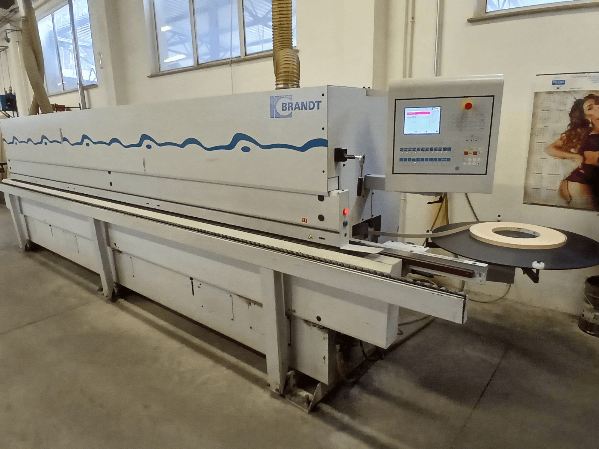 Máquina de aplicação de fita de borda Brandt, vista lateral, com um painel de controlo e um rolo de fita na mesa de alimentação.
