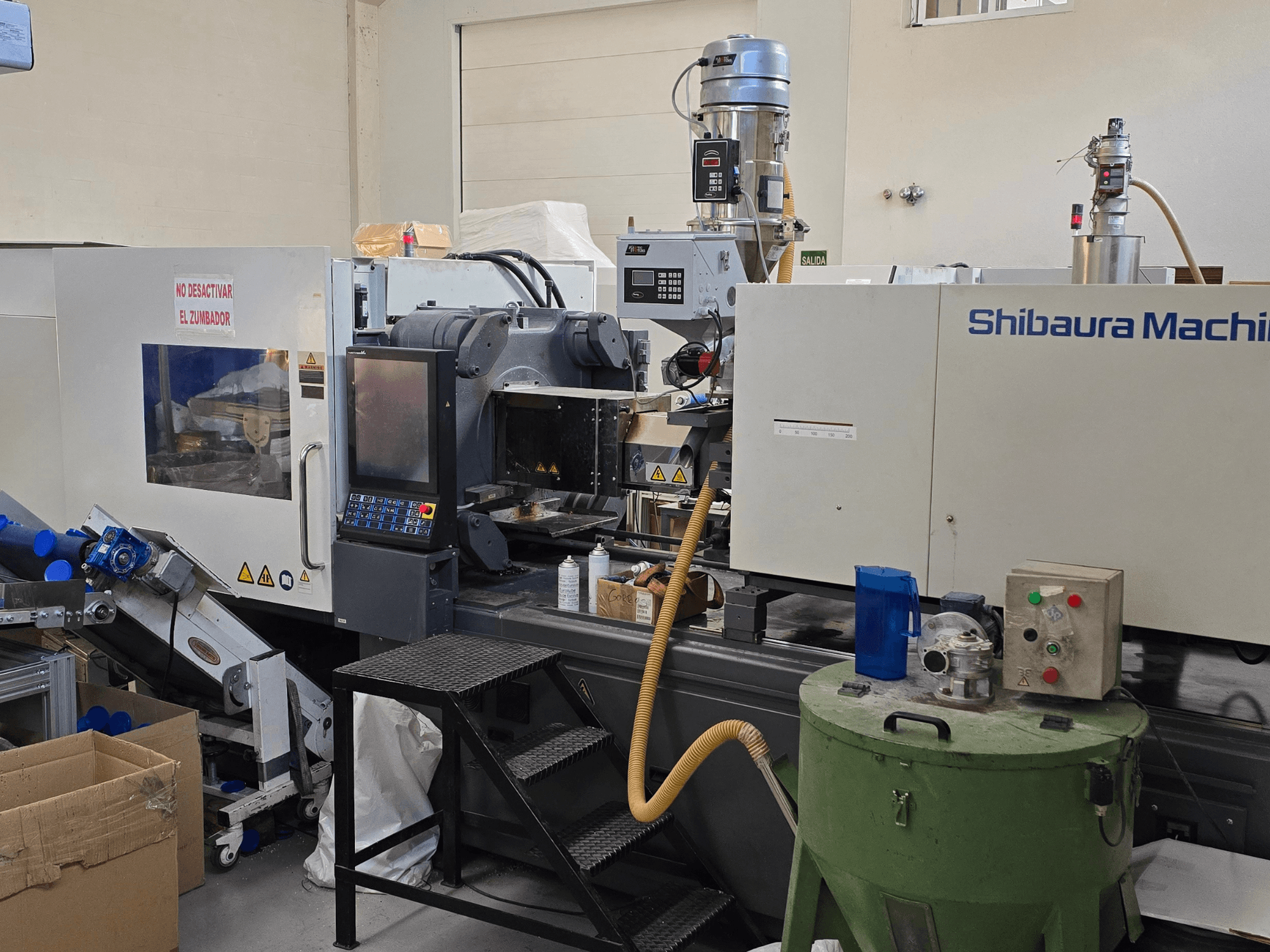 Vista frontal da máquina de moldagem por injeção eléctrica SHIBAURA EC230SXIII-8A com painel de controlo e equipamento adjacente.