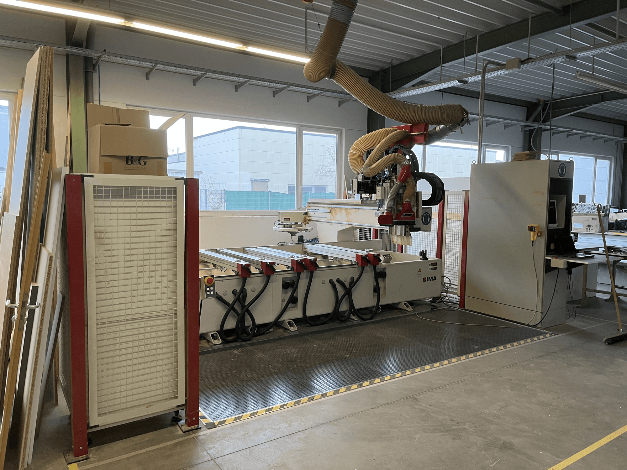 Centro de maquinação CNC para madeira IMA BIMA 410 na oficina, vista lateral com painel de controlo e sistema de extração de poeiras visível.