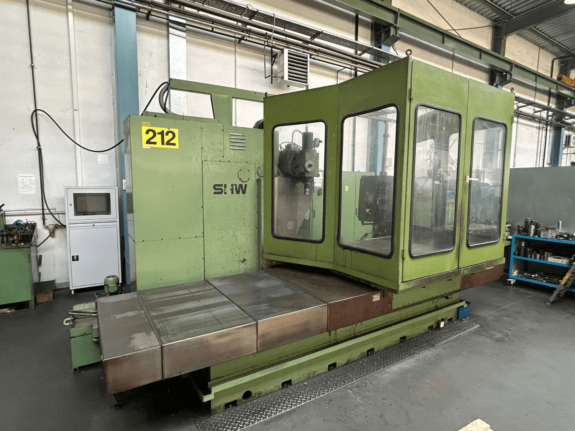 Centro de maquinação vertical SHW UF-5 em verde, vista frontal mostrando o painel de controlo, a caixa de vidro e a mesa de trabalho em metal.